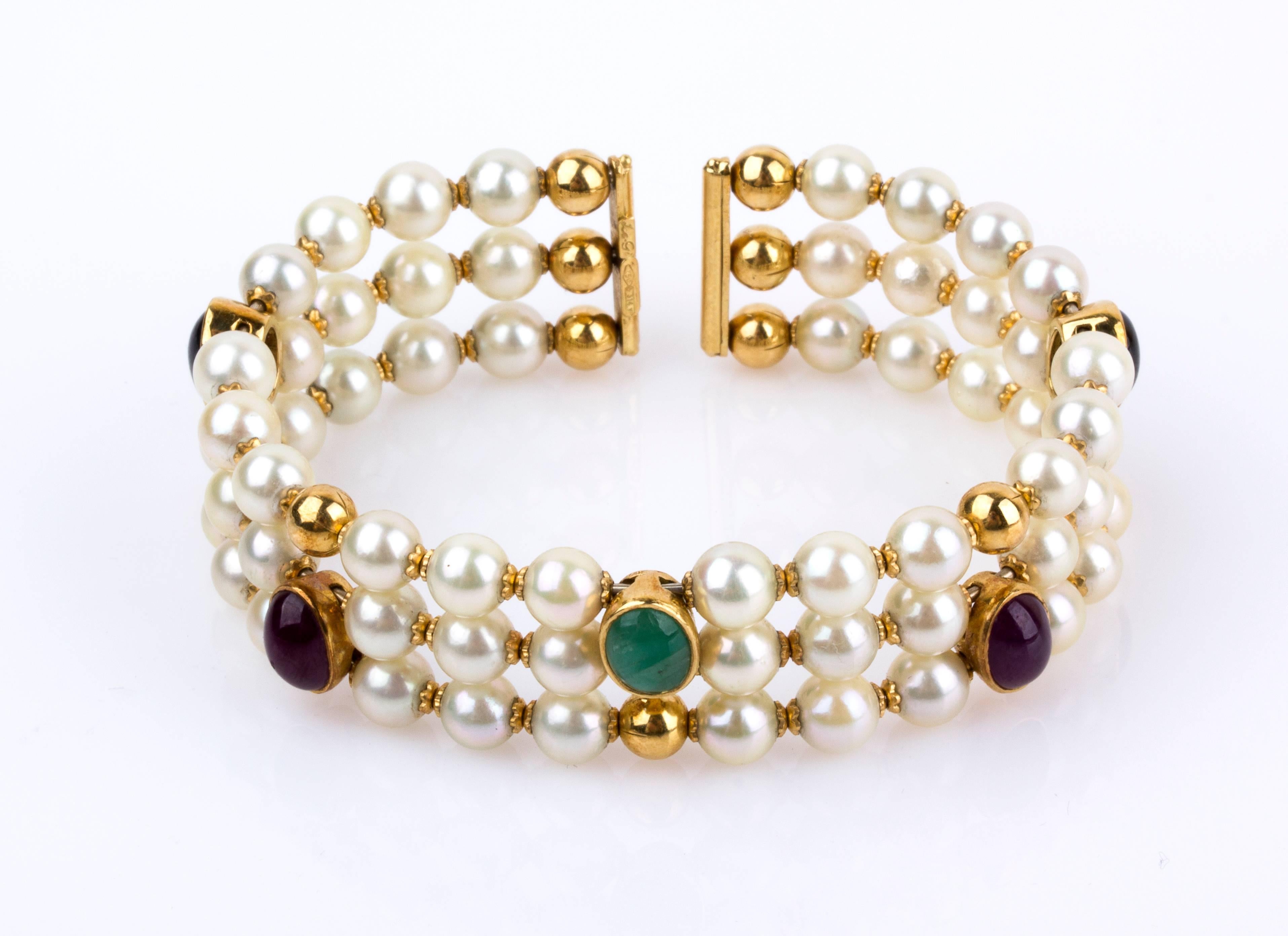 Cuff - bracelet three rows of cultured pearls, set sapphires, rubies and emeralds intervallated by jellow gold boulles. Pearl diameter 5.5/6 mm. Diameter 52 mm. Weight 33.6 gr. Italian assay mark 750 and marker's marks. Item condition grading: ****