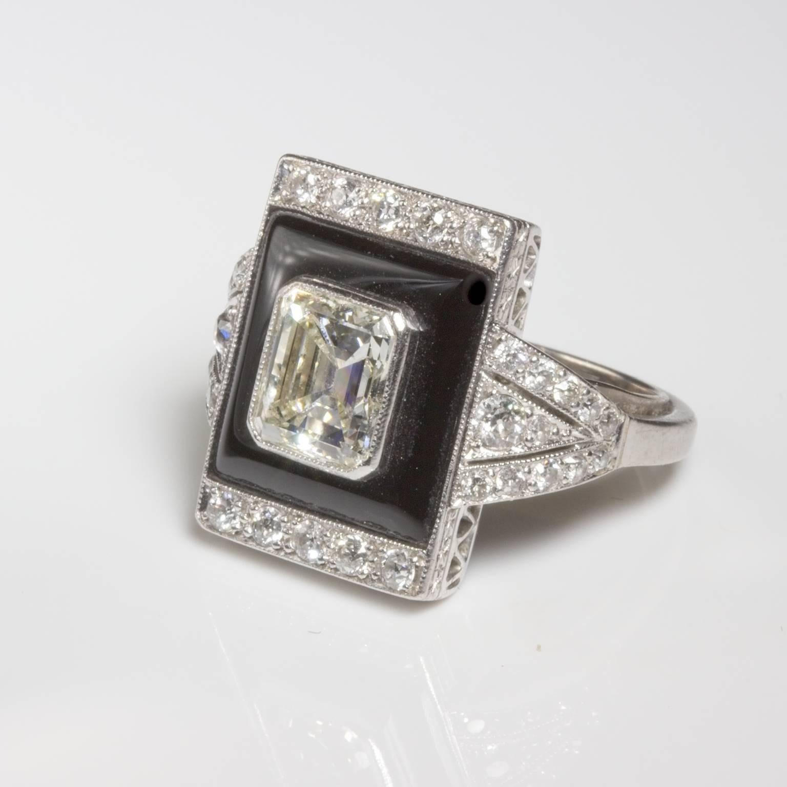 Art deco platinum onyx and diamond cocktail ring featuring a 1.74ct emerald cut centre diamond surrounded by 0.88ct round diamonds including tapered diamond set shoulders. Classic art deco black and white contrast between the onyx and diamonds.