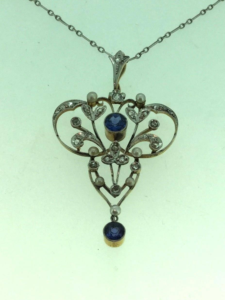 Classic antique Belle Epoque pendant set with 2 round medium blue sapphires surrounded by 7 seed pearls and 24 rose cut diamonds and an old cut and rose cut diamond set in an articulated bale. The pendant has a fine platinum top plate and 18 carat