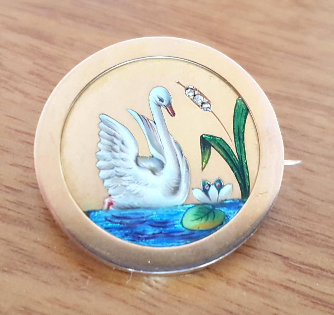 Pretty and elegant, this round brooch in 18ct gold features an enamelled swan with iridescent water, lotus flower and bloom containing 3 old cut diamonds. Diameter 3cm.