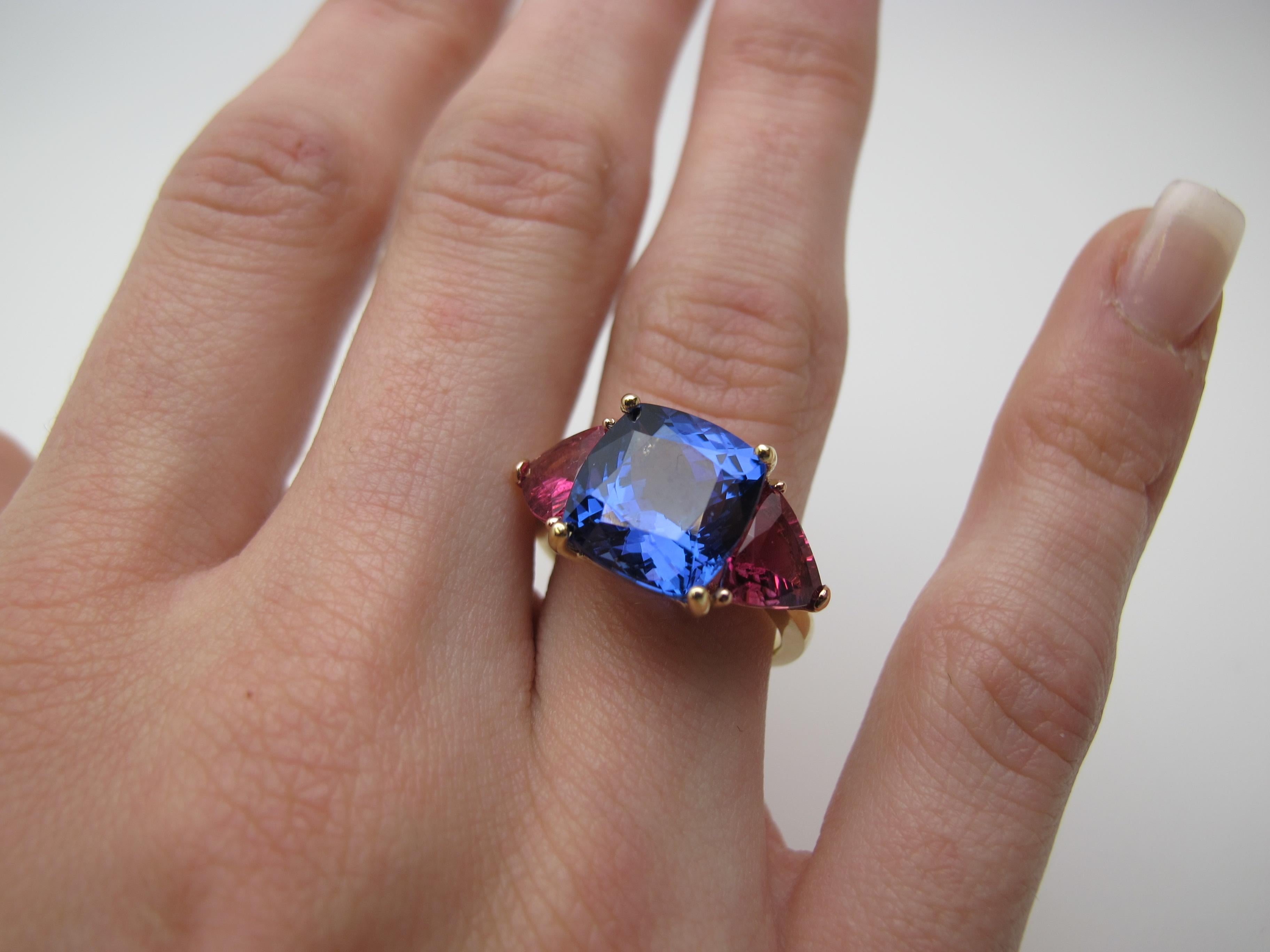 We have combined a beautiful lavendar-blue tanzanite with fuschia colored tourmalines to create this unusual color pairing. The stones contained by  this custom ring are gems in every respect: fine color, clean and well cut.  The tanzanite is 