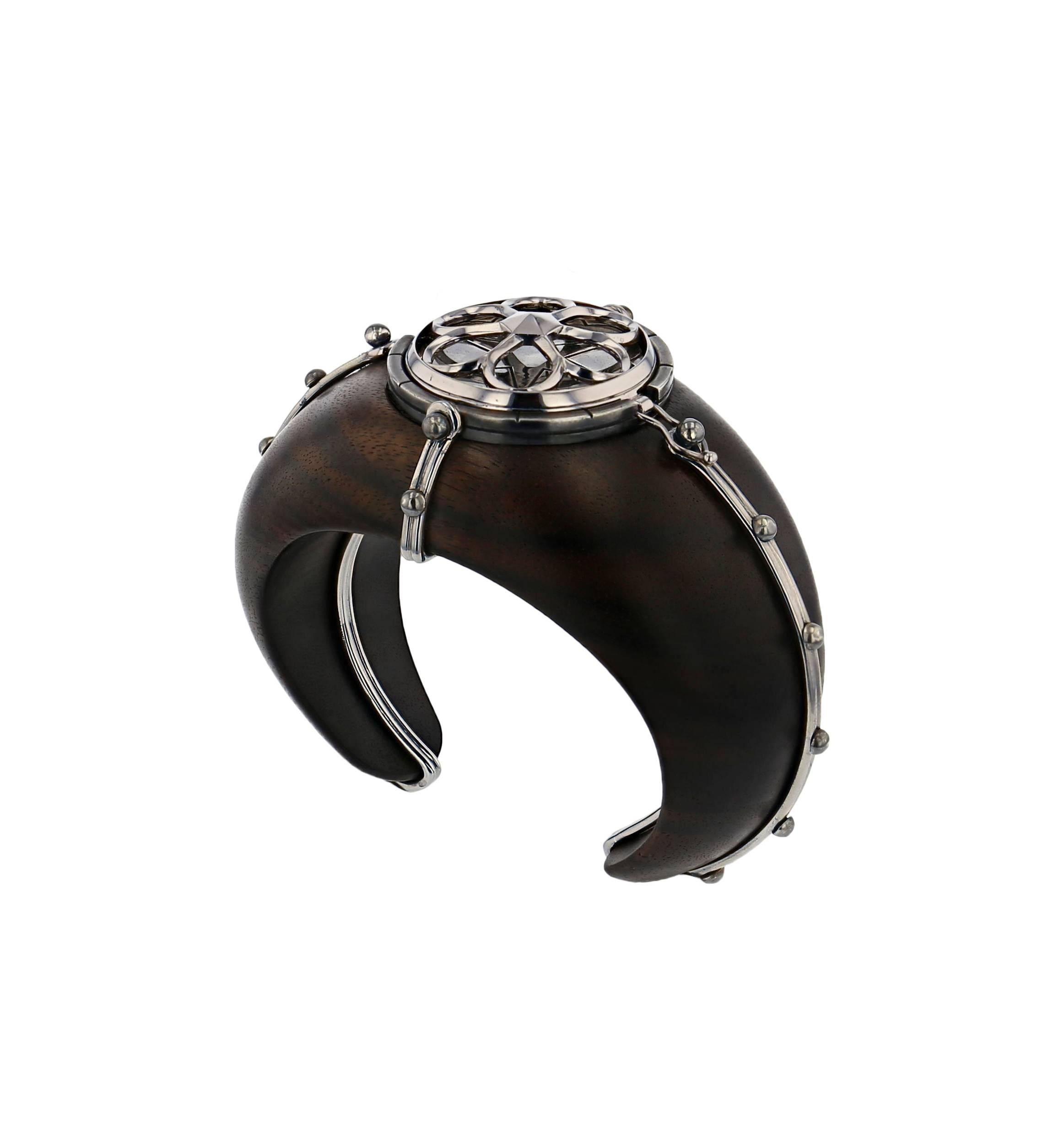 Desdemone Cuff Ebony 18 Carat White Gold Rubelite Lapis Diamonds

This large cuff is sculpted from Macassar ebony within a gold cage. At the centre, a pivoting sphere shows a white gold rosette on patinated silver when closed, and opens up to reveal