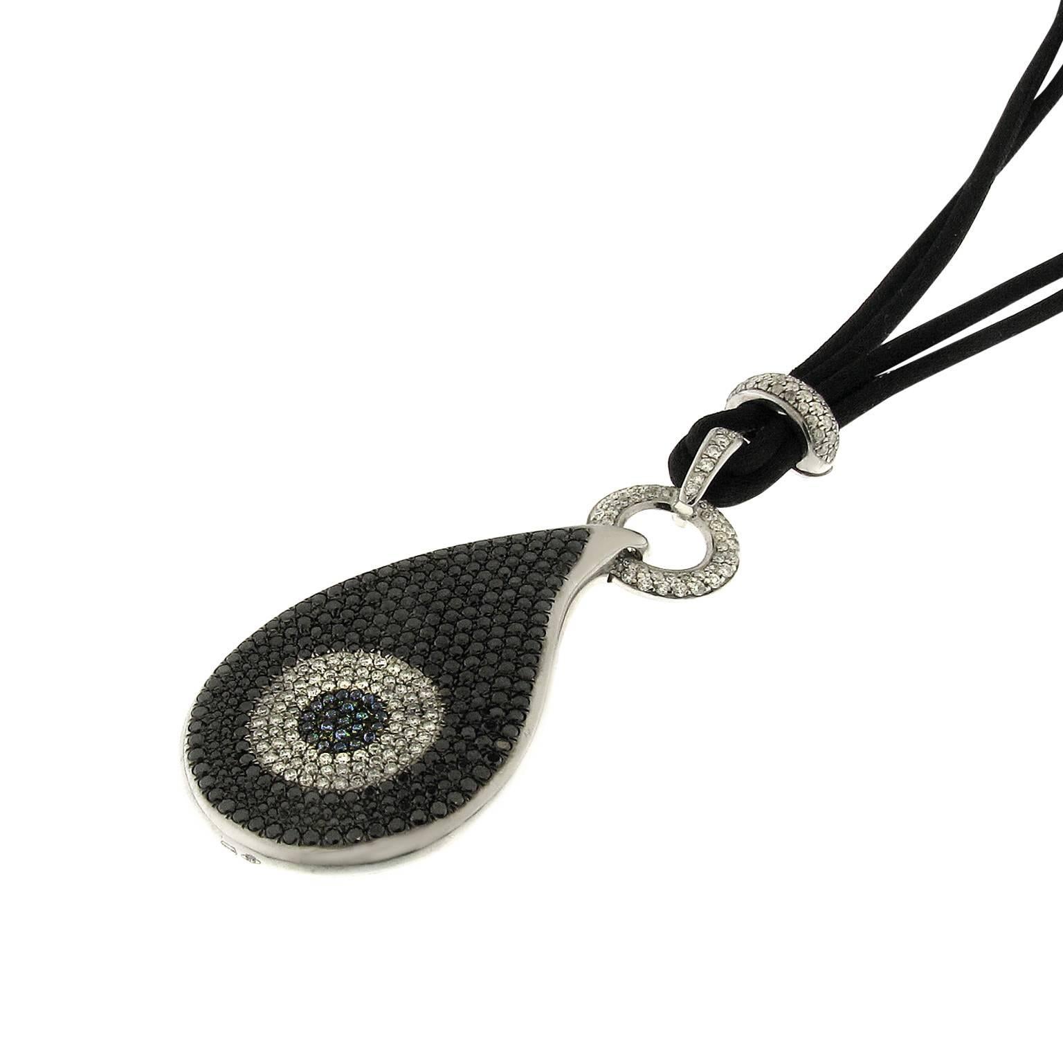 Timeless contemporary evil-eye sculptured pendant in 18k white gold. The jewel features a black and white diamond and tanzanite pavé setting. Total diamond weight is 6.16ct. The pendant is mounted on black silk cord and lined with onyx