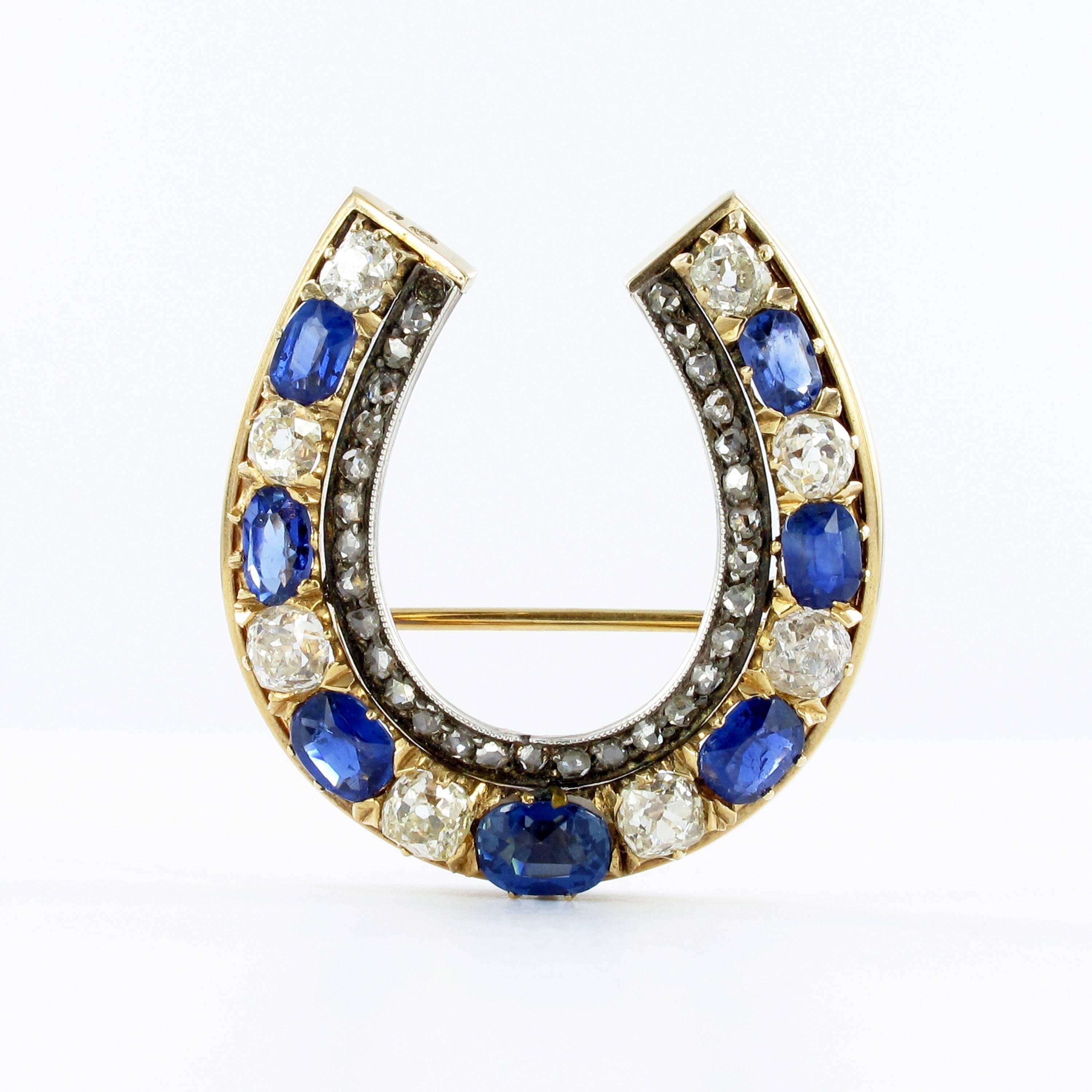 Designed as a horseshoe, this pendant/brooch in 14k yellow gold and silver features seven cushion shape sapphires and eight old mine shape diamonds. Total estimated weight of 4.50 carats for the sapphires and 2.70 carats for the diamonds. Inner