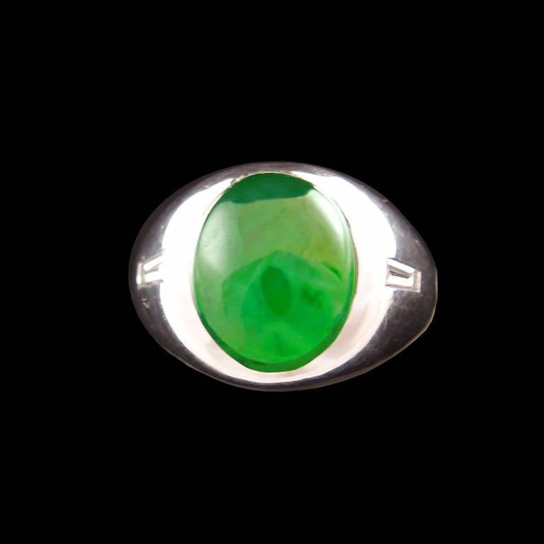 A heavy platinum ring featuring a  large, natural jade cabochon, of deep green color, with good translucency, and flanked on either side by baguette cut diamonds. Ring size 9.

Stamped with a maker's and platinum mark.