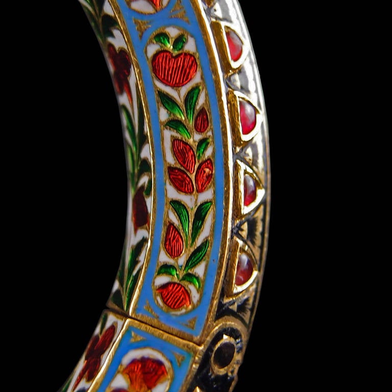 A fine Indian 18th century Mughal 22k gold bangle with kundan set diamonds and rubies, featuring fine enamel work.

The enamels bold an bright with abstracted floral and fruit designs in shades of red and green against blue and white enamel grounds.