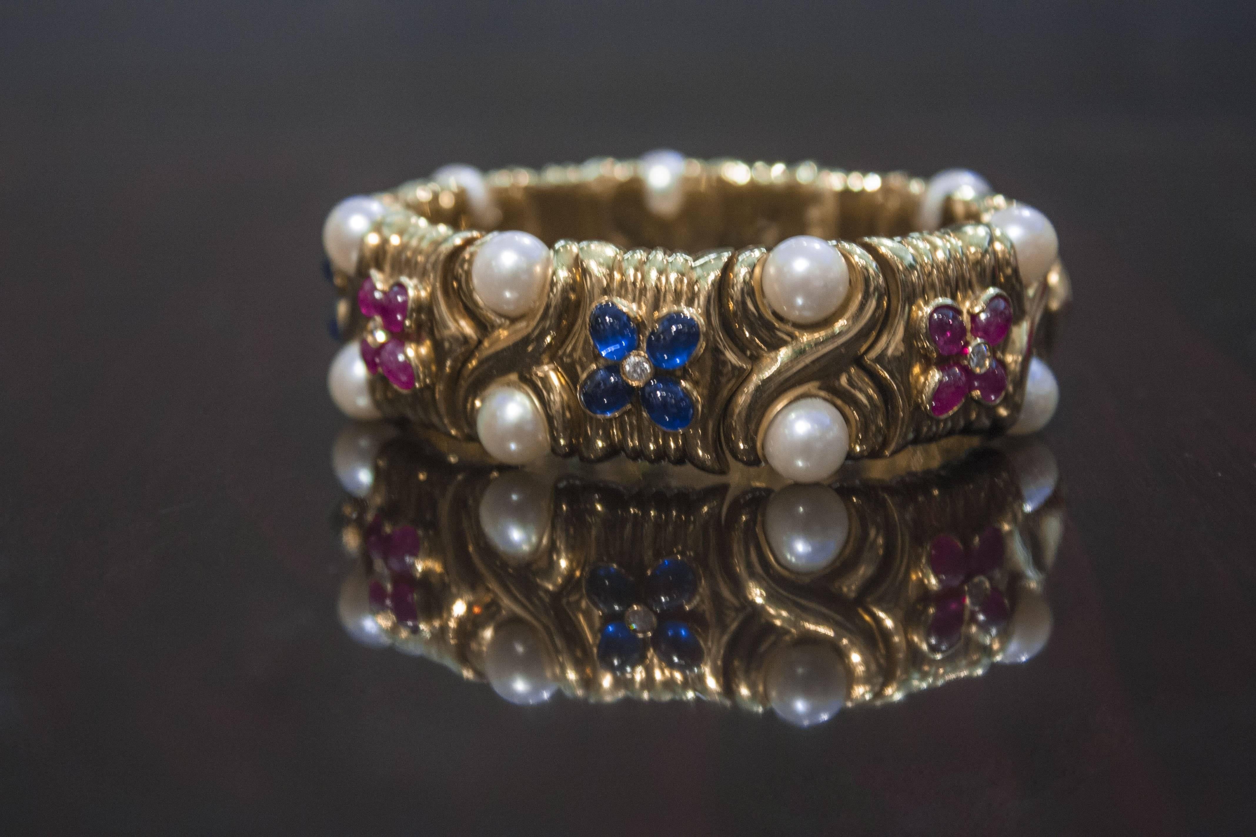 A beautiful and classic flexible 18K yellow gold cuff bangle set with pearls, sapphires and rubies by Bulgari, circa 1980's. 

The bracelet masterfully worked in 18k gold with flexible links and set with pearls, rubies and sapphires. The rubies and