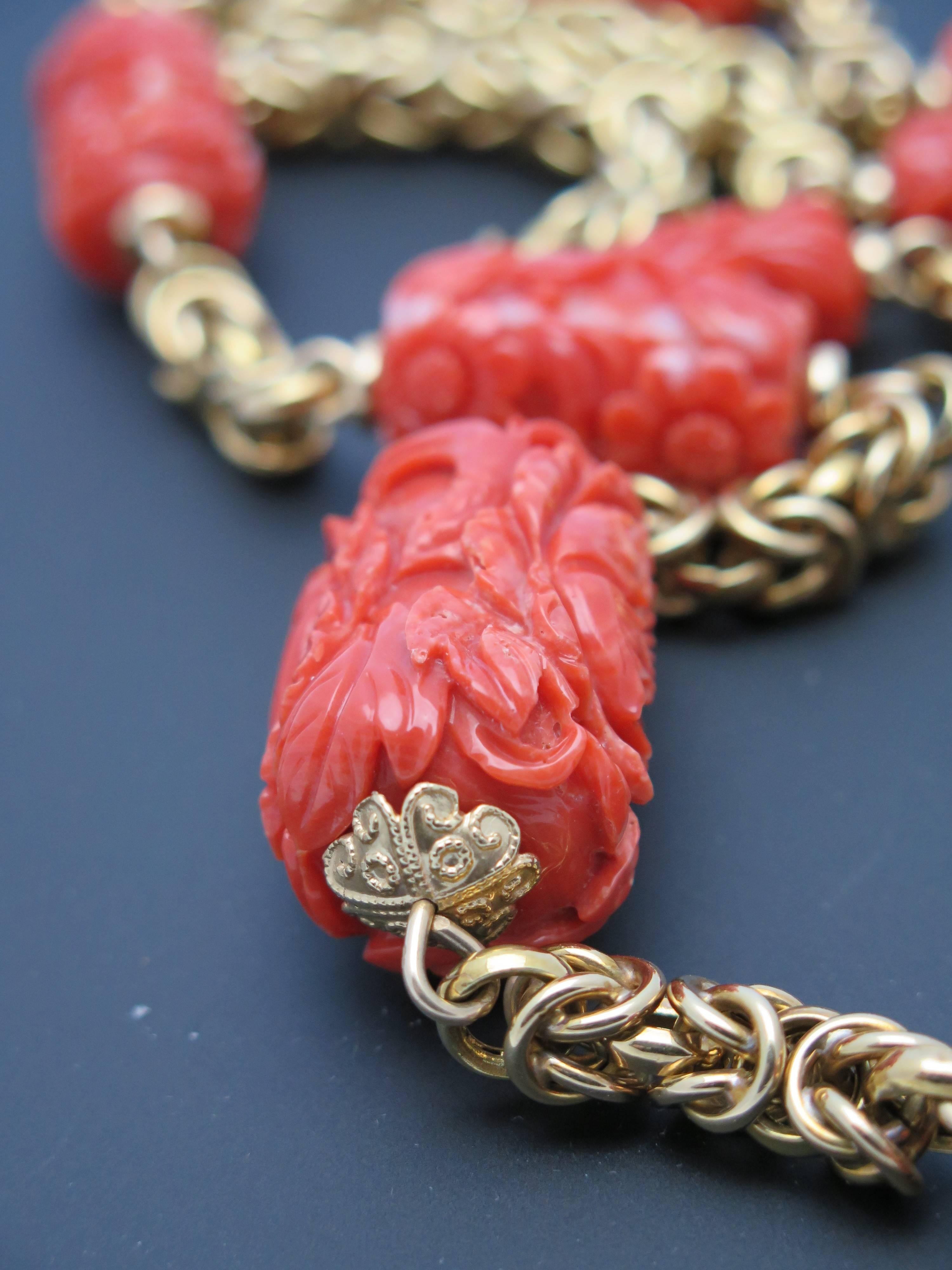 Featuring 11 graduated, oversized cylindrical carved coral beads on a chunky 14k yellow gold Byzantine chain. Each bead is of an overall deep salmon color, and carved with an intricate floral motif. 

The larges bead measures approximately 33mm x