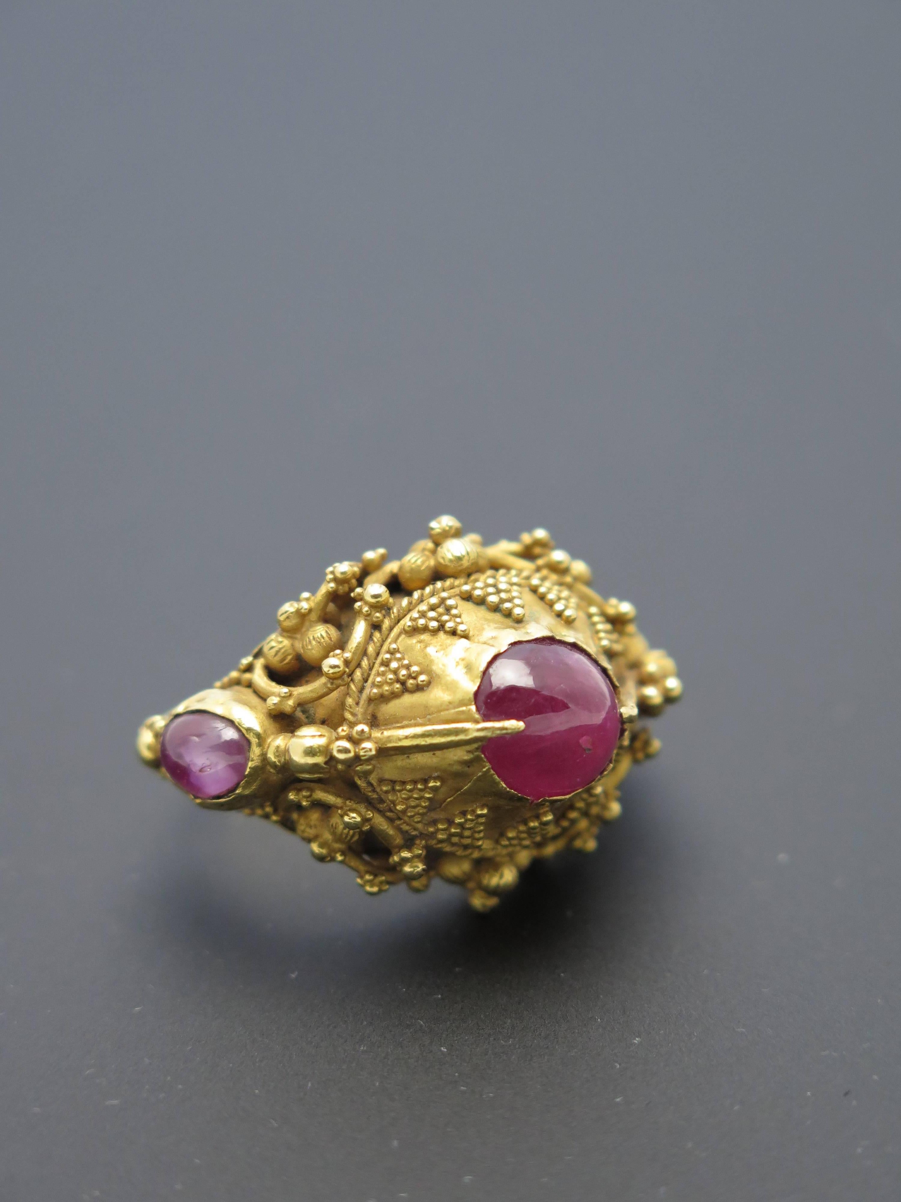 Finemente lavorato in oro ad alta caratura (22k+), presenta tre rubini cabochon tagliati a vivo che vanno dal rosa chiaro al rosa violaceo, tipico dei rubini dell'Indonesia. Meravigliosa granulazione e dettagli scultorei.

Anche se di forma