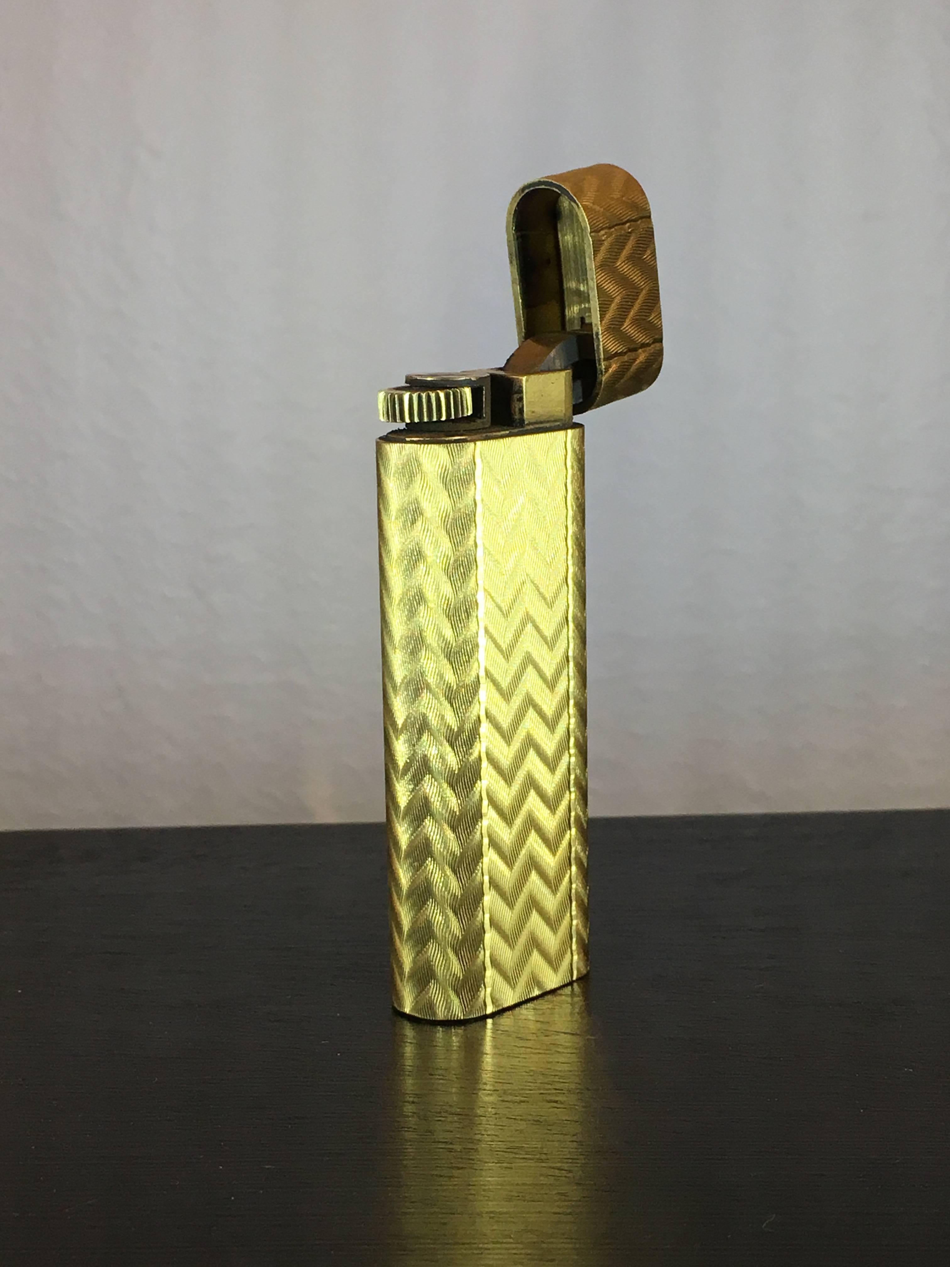 A gold plated lighter in a textured chevron pattern, signed Cartier Paris. 
With original box.