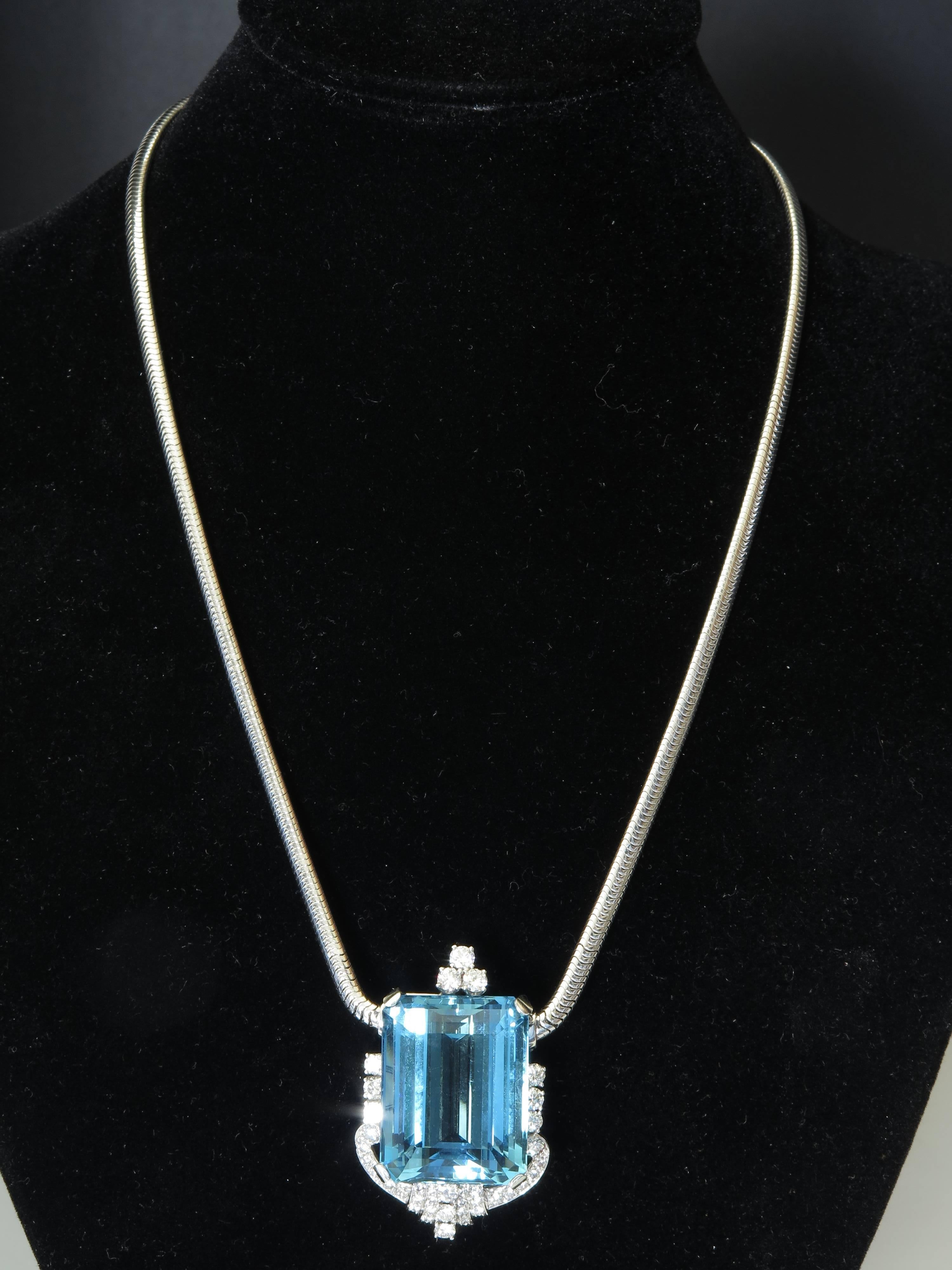 A large and impressive aquamarine pendant mounted in platinum and surrounded by diamonds, all suspended from a 14k while gold serpentine link chain.

The bold rectangular step cut aquamarine of highly saturated deep blue color, weighing