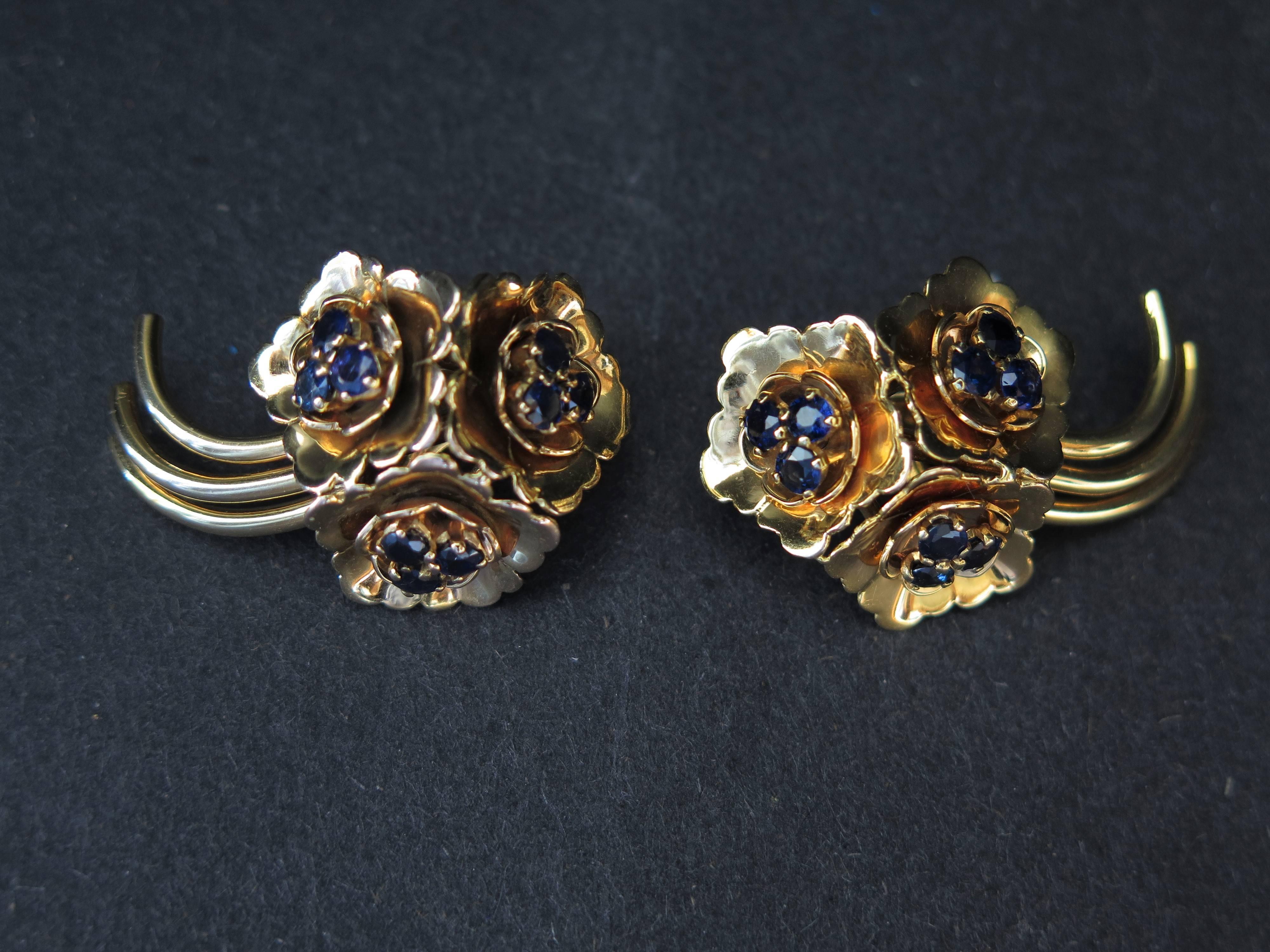A lovely pair of 1950's Retro earrings by Kutchinsky. 
Each clip earring is fashioned as a group of three flowers with long, curved stems. Each en tremblant open blossom featuring three stamen of blue sapphire. 
Signed Kutchinsky. 