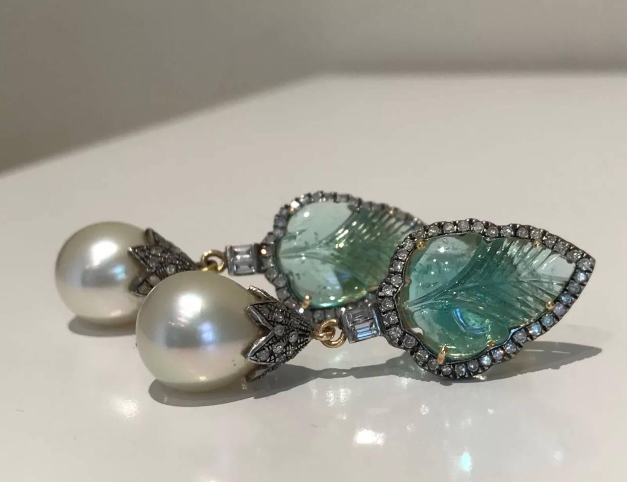 A Pair of Emerald, Diamond and Pearl earrings set in 14k yellow & white gold. Each earring features an emerald engraved in the shape of a leaf with a surround of thirty five brilliant cut round diamonds and two emerald cut diamonds with a tassel