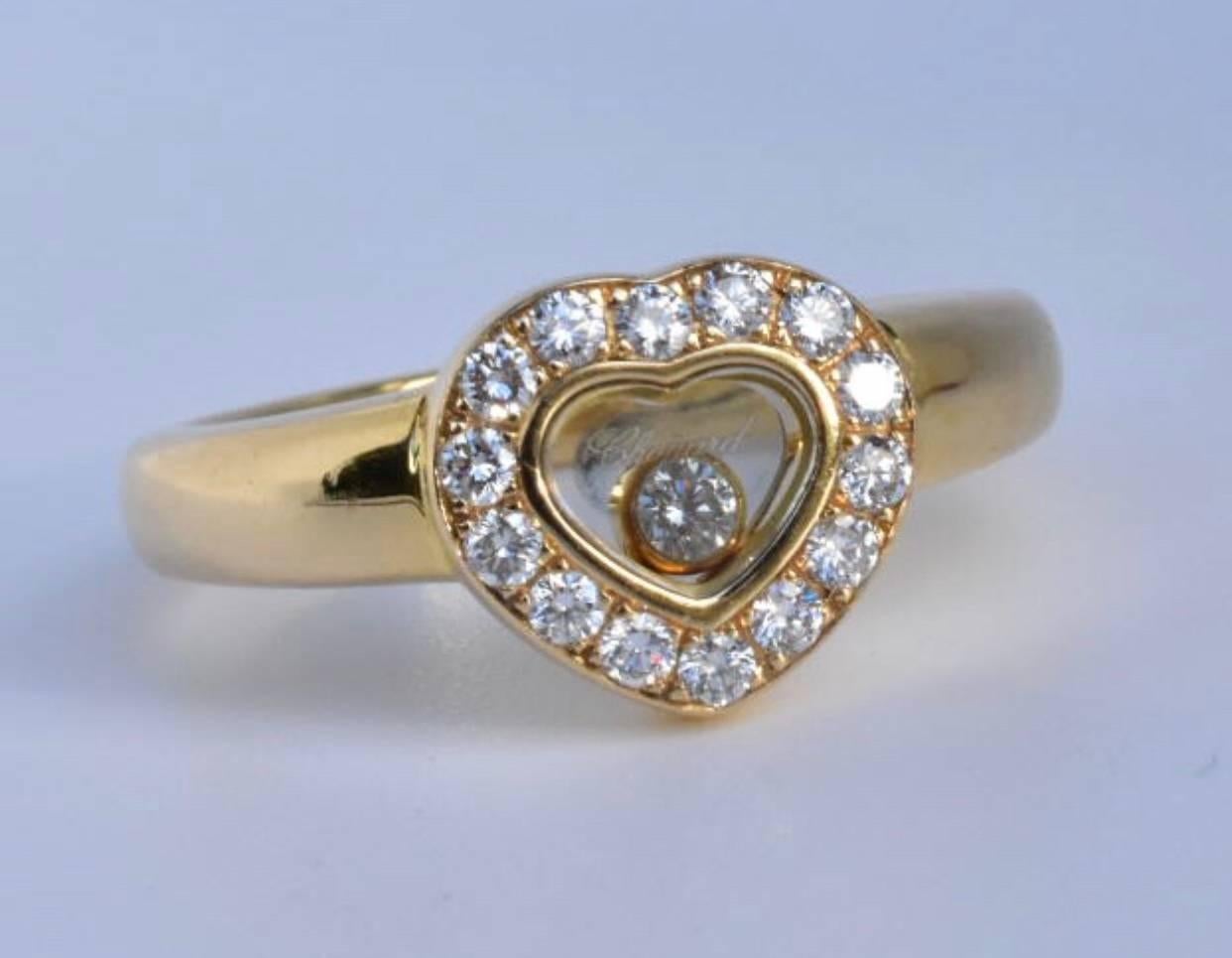 A Chopard Happy Diamond ring set in 18k yellow gold. The ring features one free moving brilliant cut diamond under a sapphire glass of approx 0.05 carats and has fourteen brilliant cut round diamonds with the heart design.
The ring is sold with the