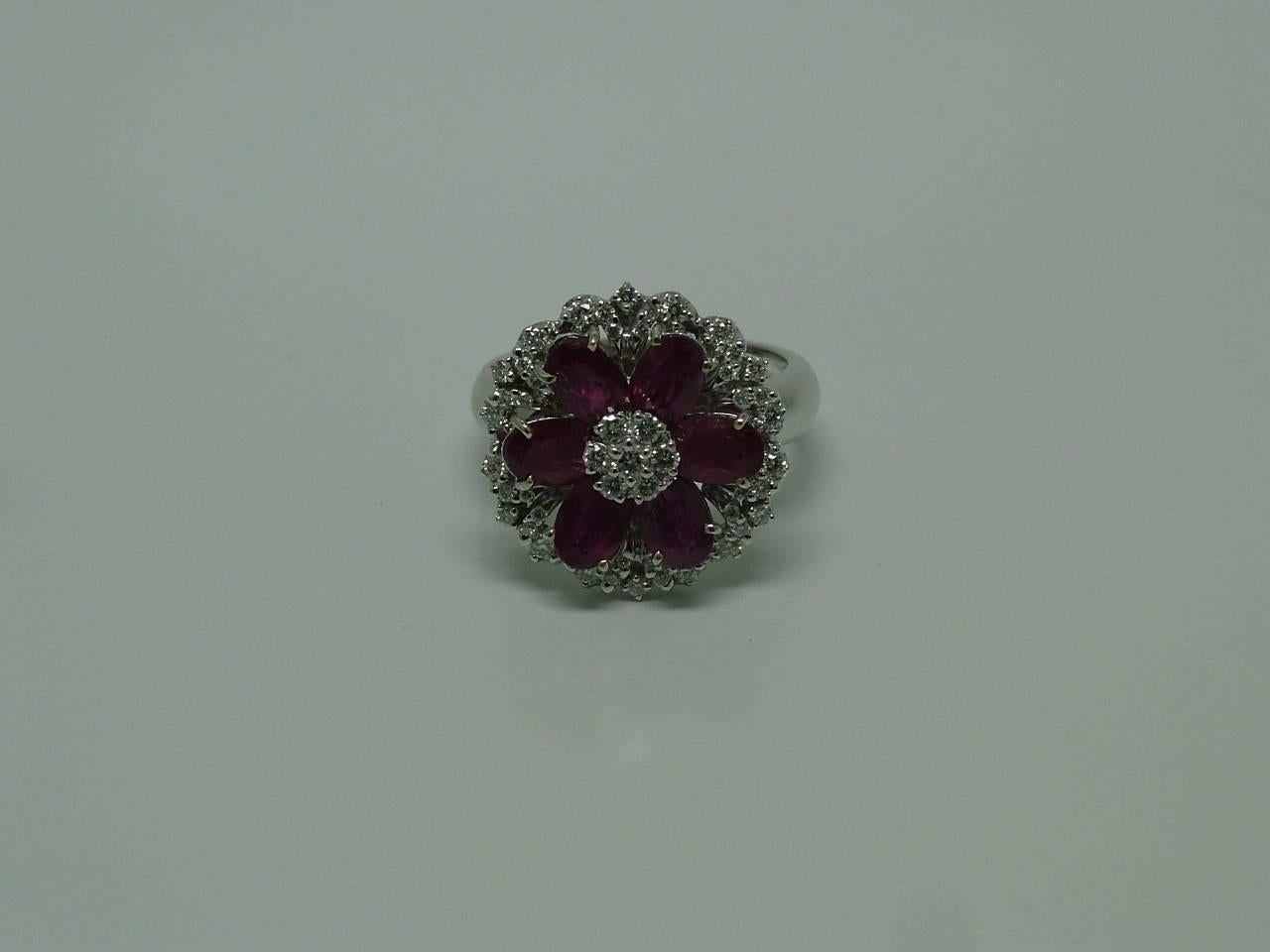 A diamond ruby cluster ring designed as a flower where petals are oval shaped rubies within a surround of diamonds.

MEASURES: 
Front measures: 17mm (frontis)
Internal diameter measures: 17,6 mm

SIZE: 
 15 EU - 7.25 US
Ring sits approx. 