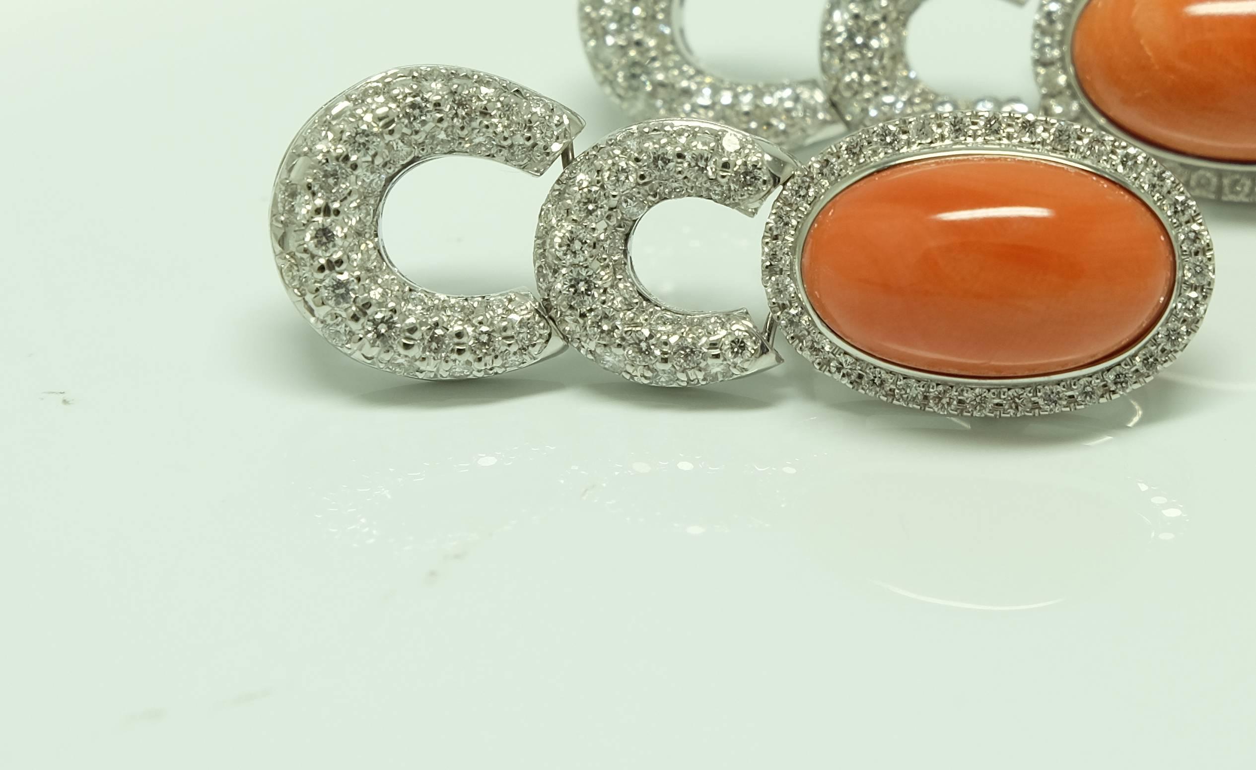 Of flexible design, this elegant pair of ear pendants feature central oval cabochon bright orange coral within a brilliant cut diamond pave set surround, with two diamond pave set crescent suspensions.
