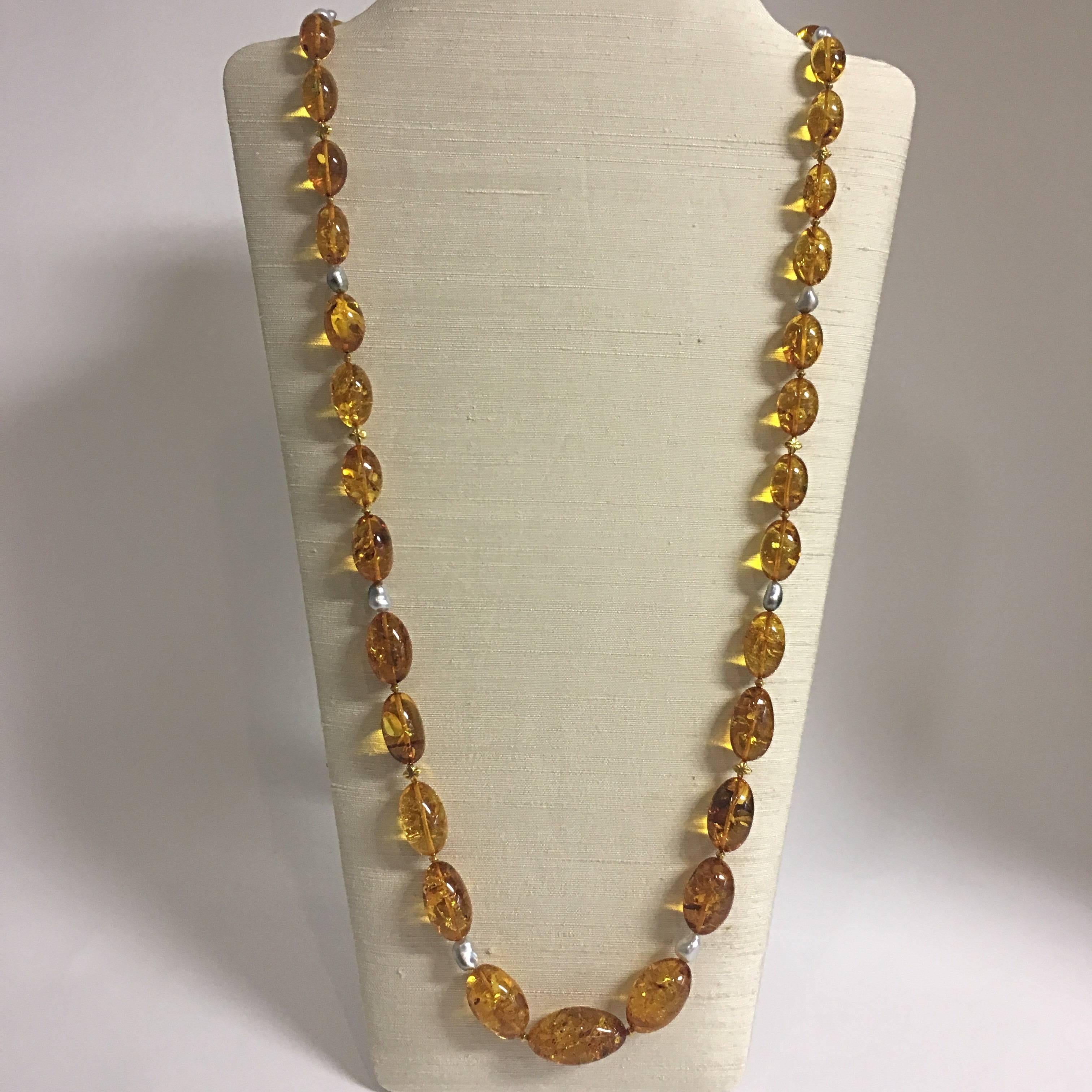 A charming 39”L (99cmL) necklace with graduating oval Baltic amber beads, ranging from 1/2”L (1.3cmL) to 1 ¼”L (3cmL) in honey colour, separated by baroque South Sea pearls and 18 Karat gold beads in diamond and star shapes, and 18 Karat gold clasp.