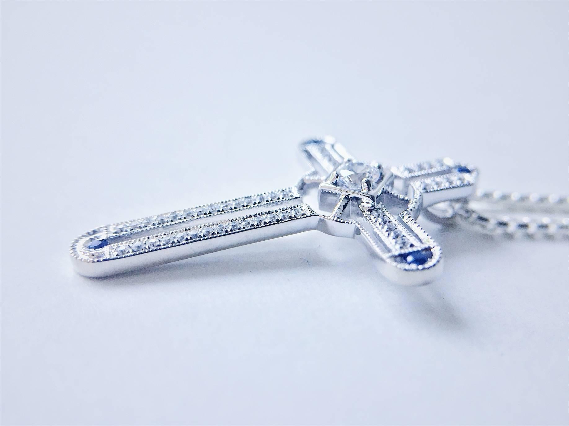 A bespoke Cross design in 9ct white gold featuring 0.68ct total of handpicked diamonds at 0.08ct of blue sapphires with fine mill grain detailing for an art deco inspired sparkle in a slider pendant. 

(Pendant comes with an white gold chain with an