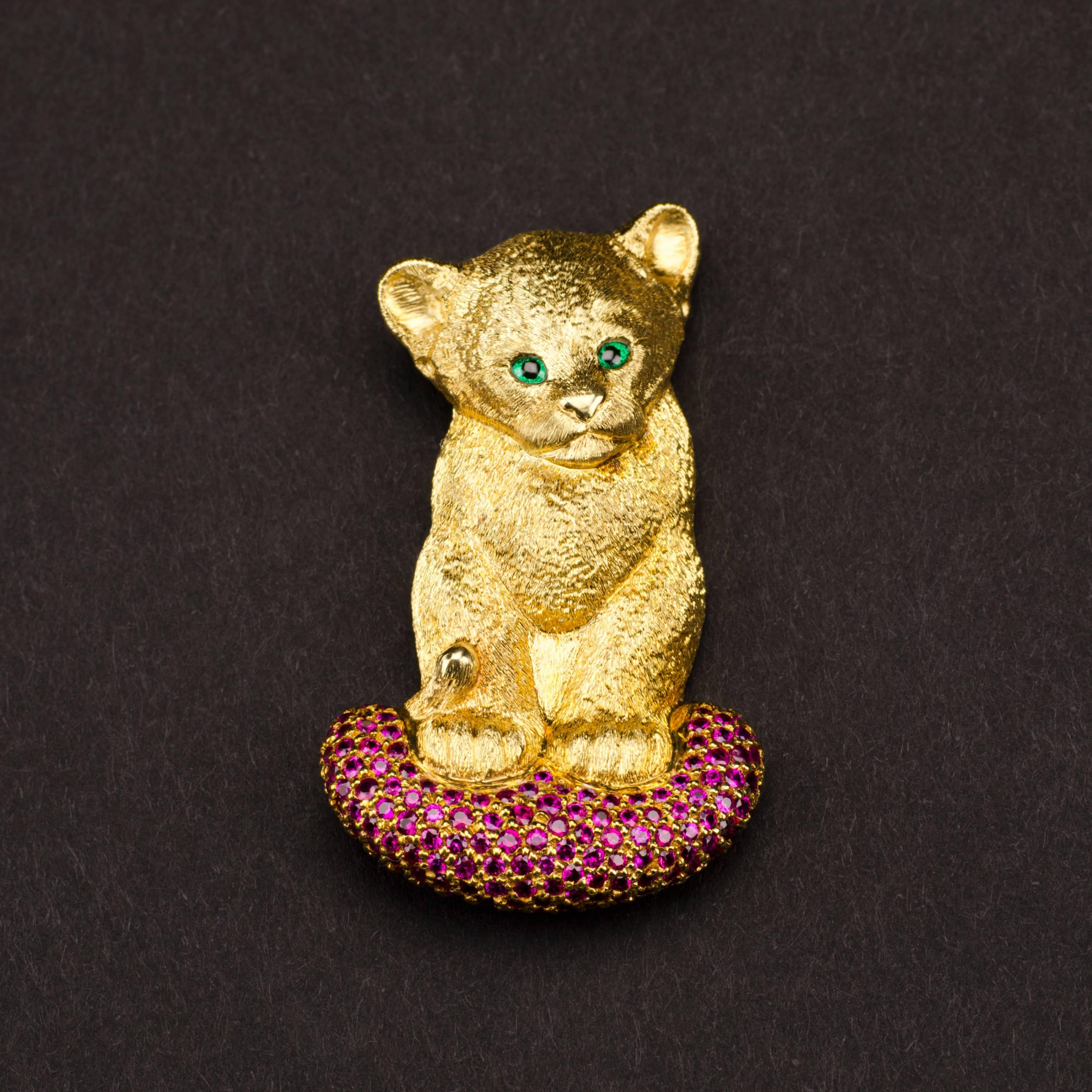 Who can resist the loving tsavorite green gaze of this endearing and extremely precious lion cub, his tail tucked around him as he sits on his ruby encrusted cushion?   

This finely sculpted 18ct lion cub brooch, which doubles as a pendant, is an