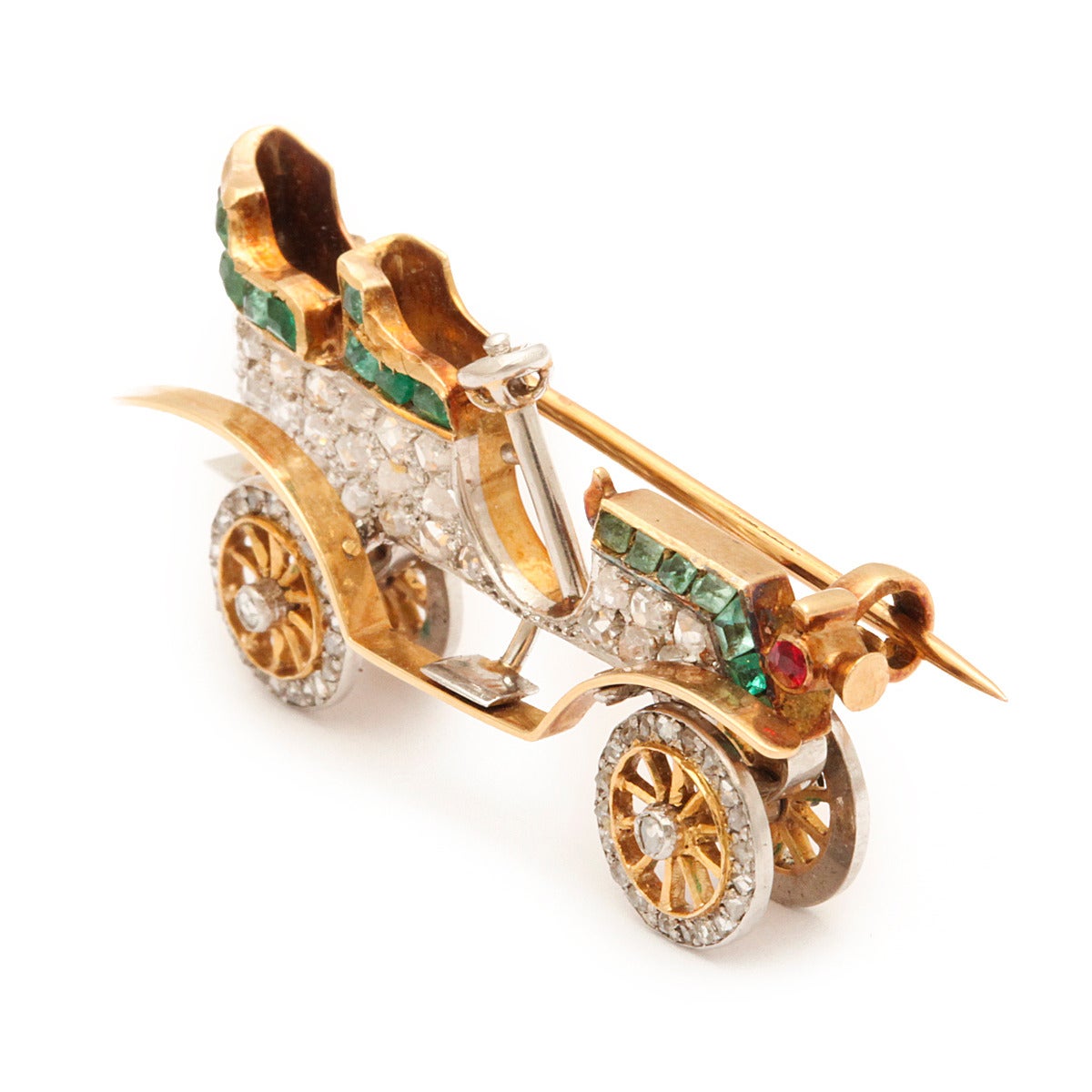 Antique brooch designed as a vintage car with pavé rose-cut diamond body, rotating diamond wheels and emerald detailing. Set in gold and platinum.