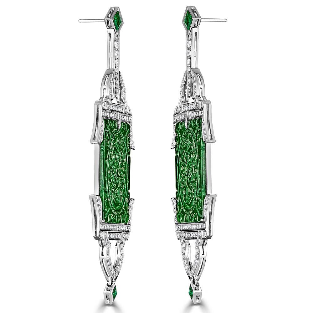 An Art Deco pair of carved Jadeite Earrings with Pave Diamonds and princess cut green Emeralds. Handcrafted in 18k White Gold earrings feature 1.76 carats total pave Diamonds. These dangling earrings feature a post and nut closure back.