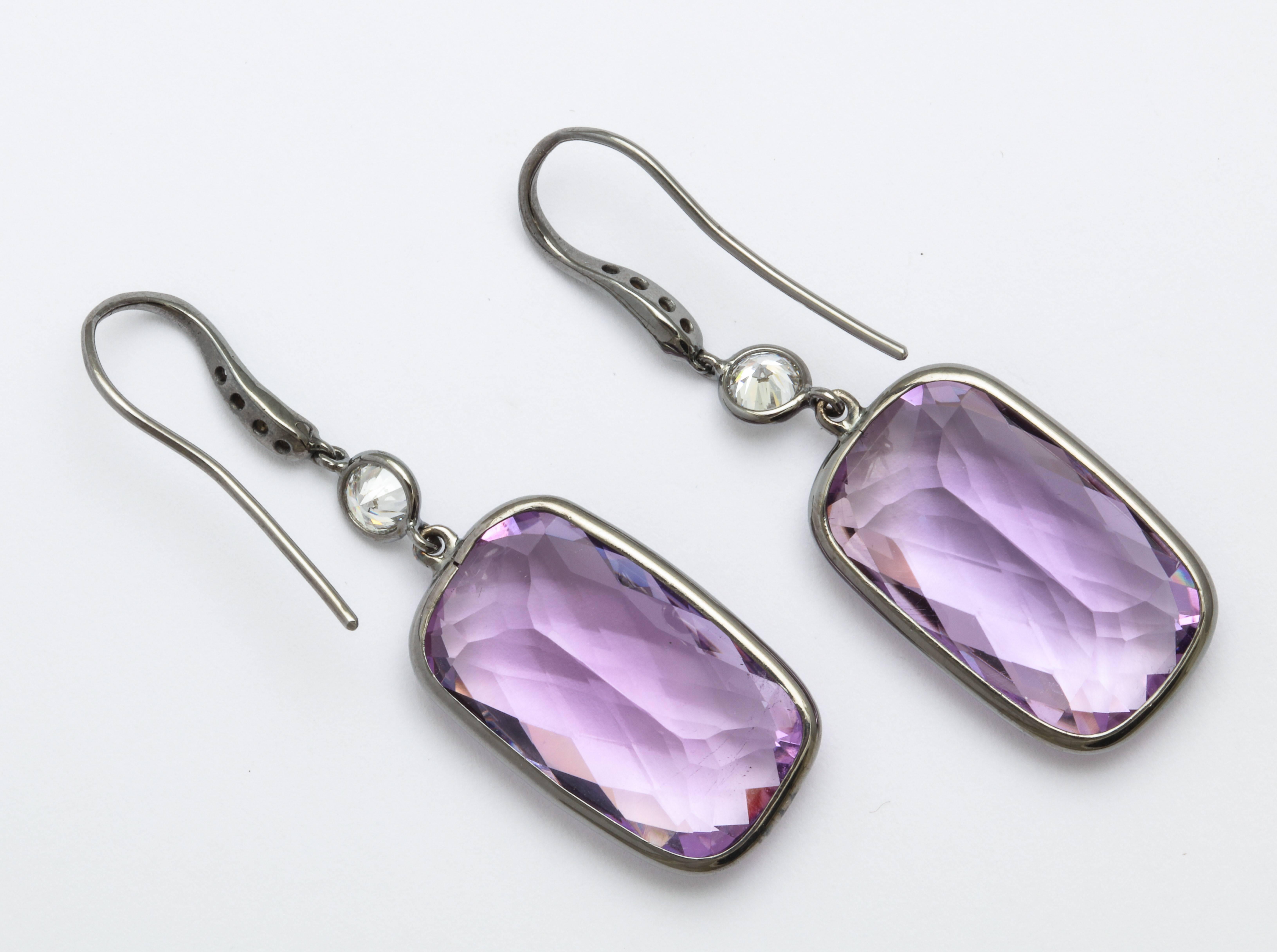 A pair of 18 karat white gold earrings, rhodium plated, with bezel set checkerboard cut amethysts, weighing 32.77 carats total. The earrings are accented with round brilliant cut diamonds, weighing 0.82 carats total. By Donna Vock Designs.