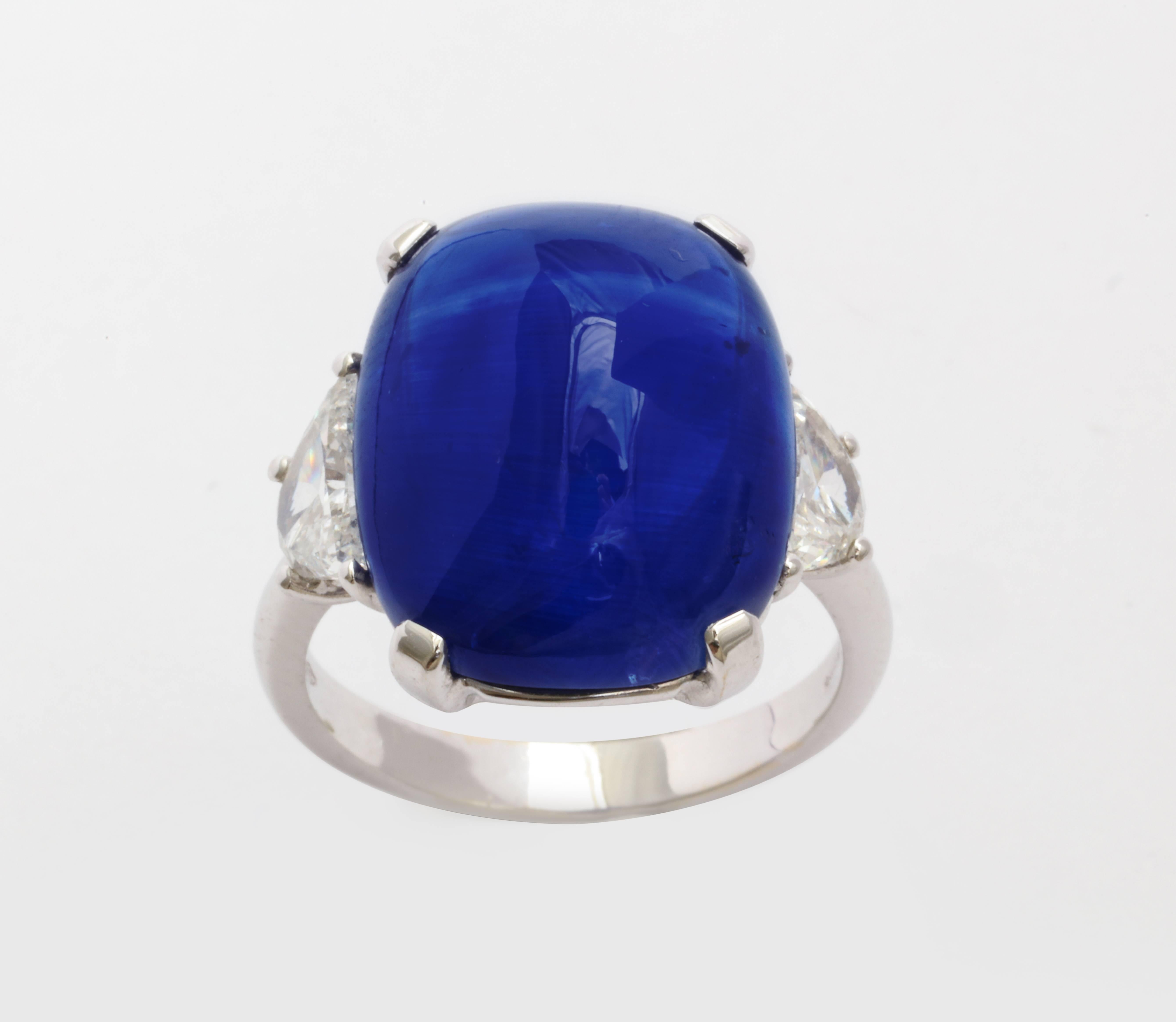 A certified heated Ceylon cabochon sapphire that weighs 18.14 carats. It is set in an 18 karat white gold ring and is flanked by two half-moon shaped diamonds with a total weight of 0.91 carats. Ring size 6.5. Certified Dunaigre CDC #1301008