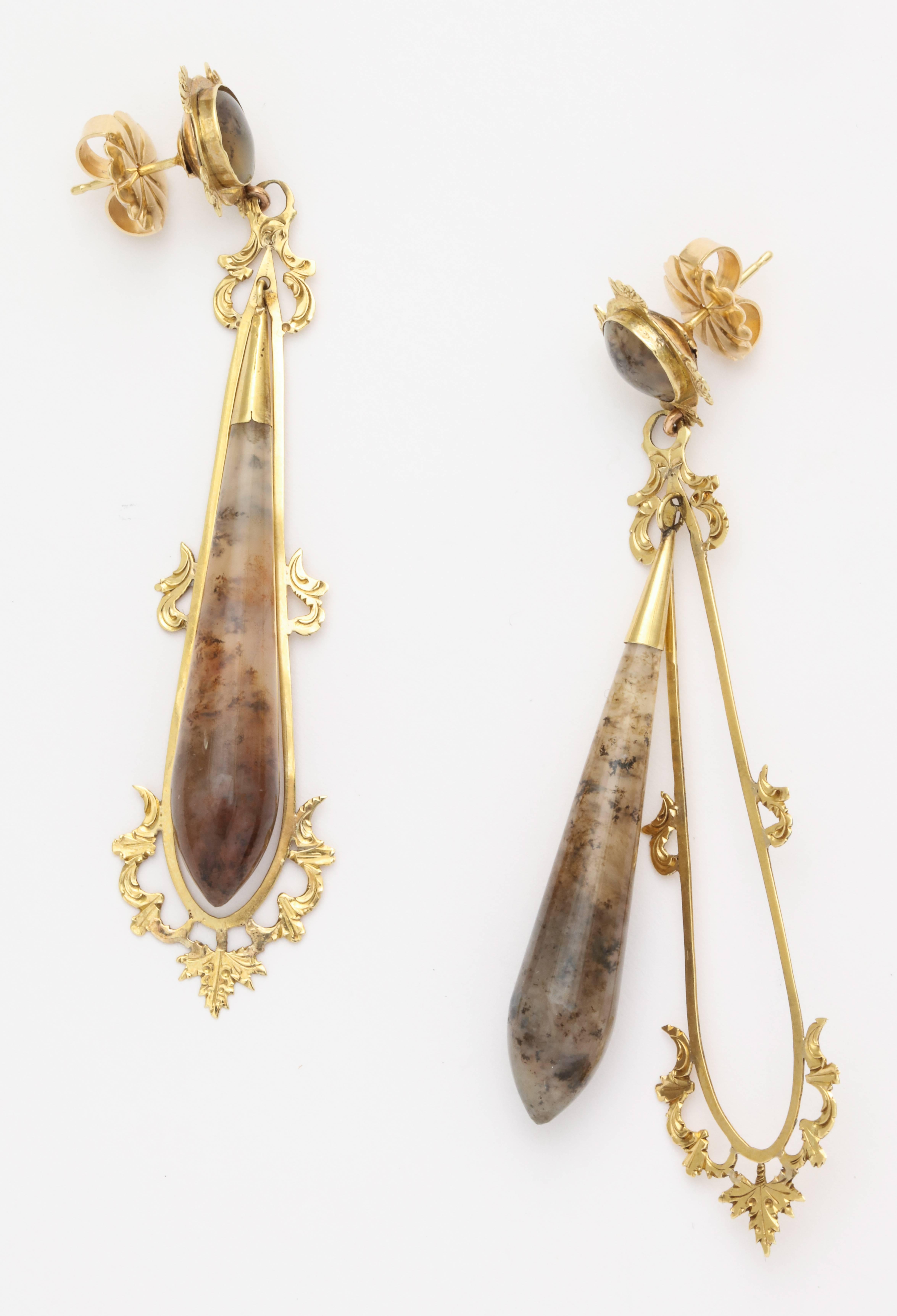 A pair of Victorian-era earrings with moss agate drops, surrounded by 14 karat yellow gold frames featuring intricate engraving and filigree work. Circa late 1800s.