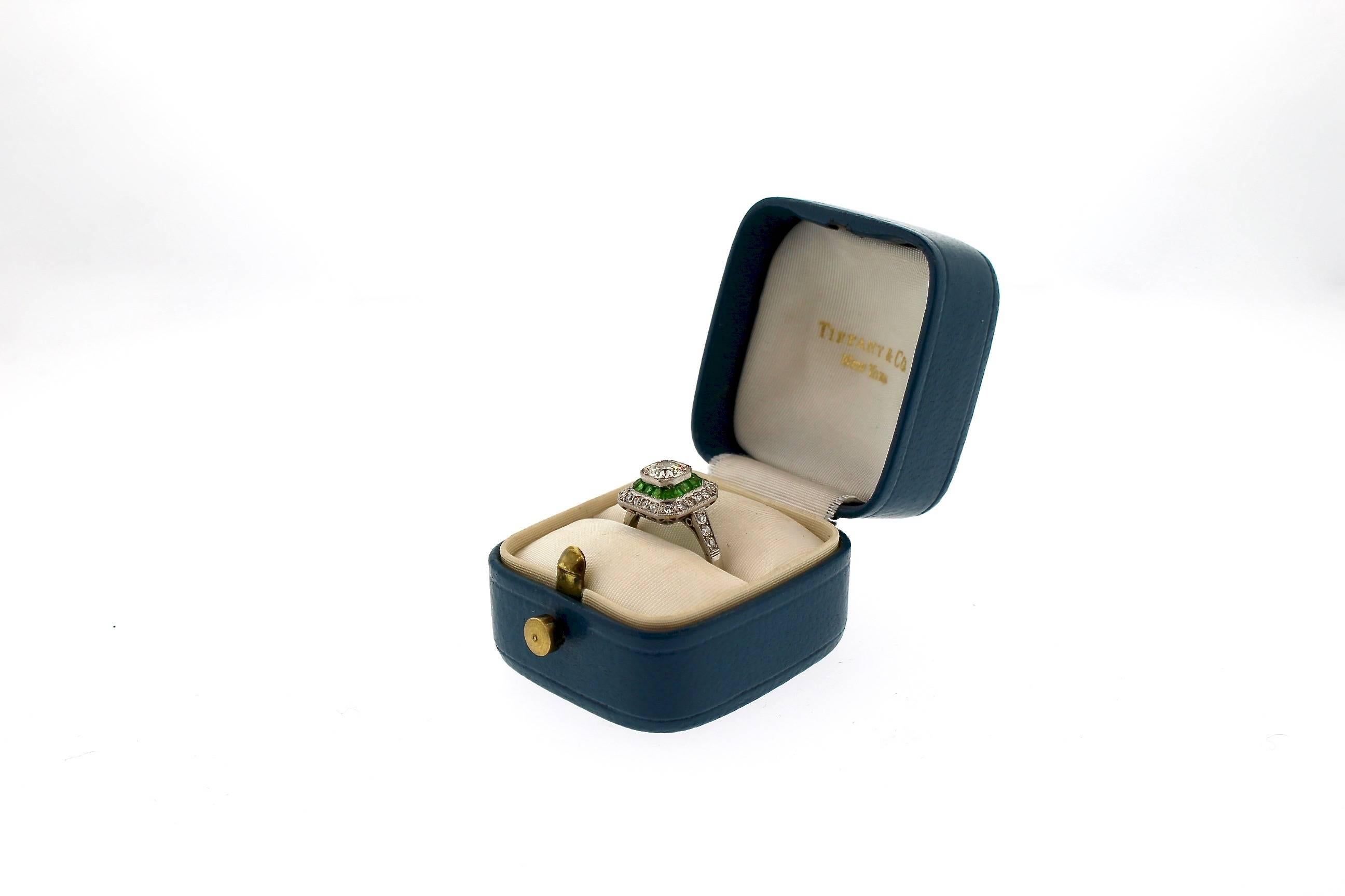 A special package for anyone!  An original Art Deco diamond platinum ring in its original box.  This ring centers on an Old European cut diamond weighing approximately 0.80 cts.  It is surrounded with calibre cut green Demantoid Garnets which weigh