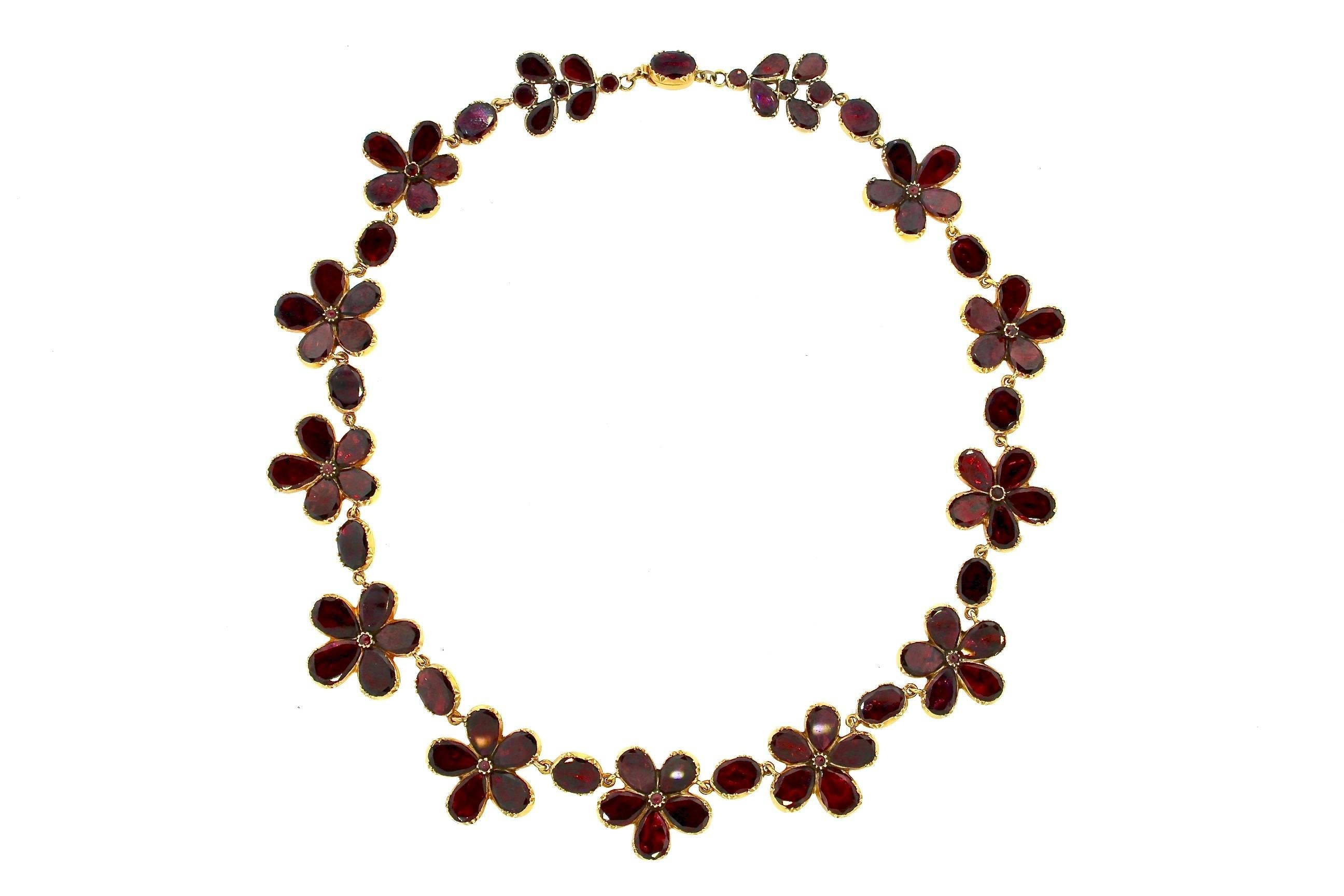 Ein feminines und lebendiges Collier, das, obwohl es über 200 Jahre alt ist, ein aktuelles und jugendliches Collier für heute ist. Rote Granate mit Folie auf der Rückseite bilden fünf spitze Blüten, zwischen denen ovale Granate eingefasst sind.
