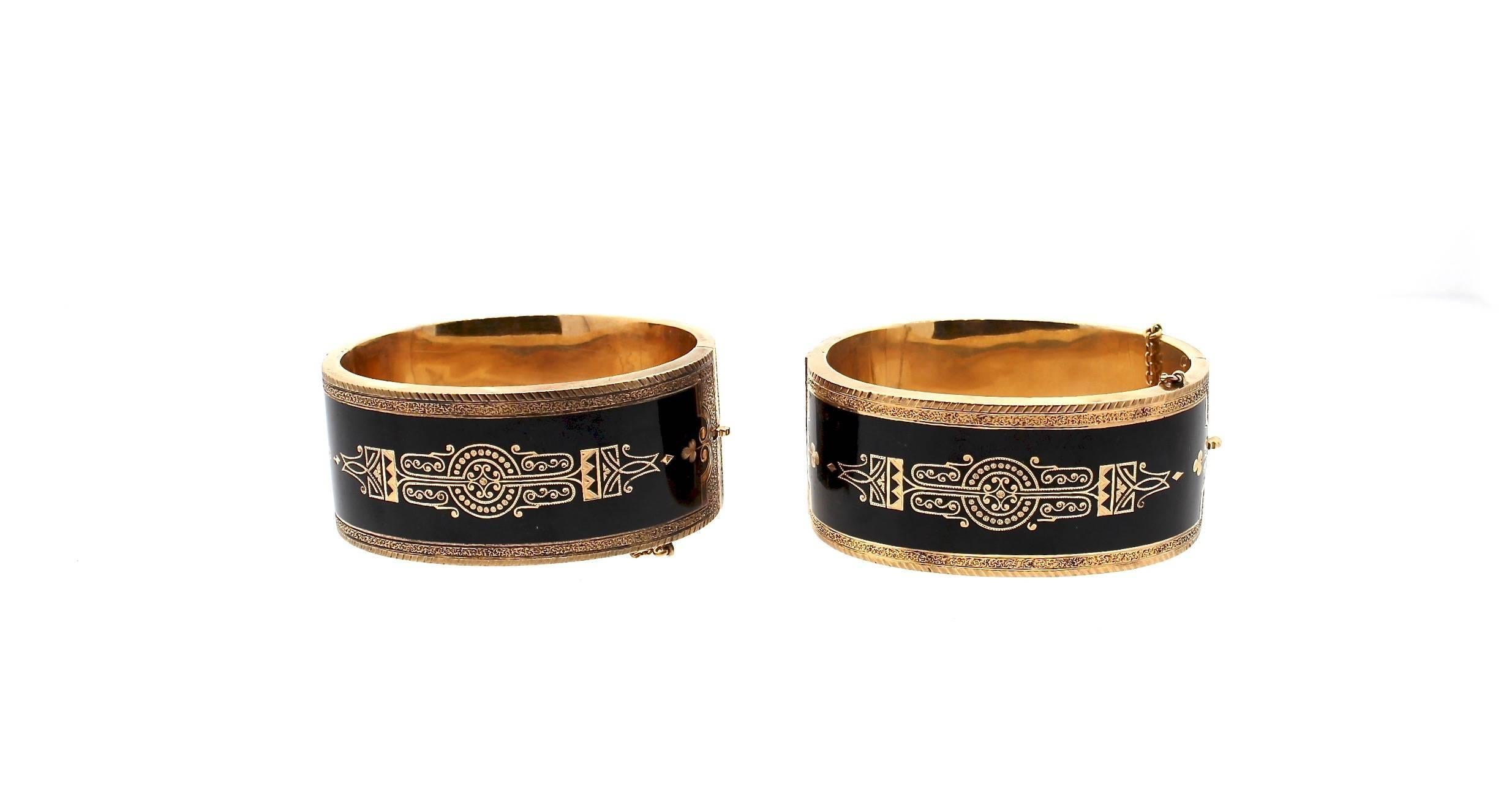 A rare Victorian pair of black enamel 14k yellow gold mourning bangles with gorgeous floral and geometric designs.  This fine pair dates to about 1860 and has floral scrollwork on one side, and a geometric design on the other.  The bracelets hinge