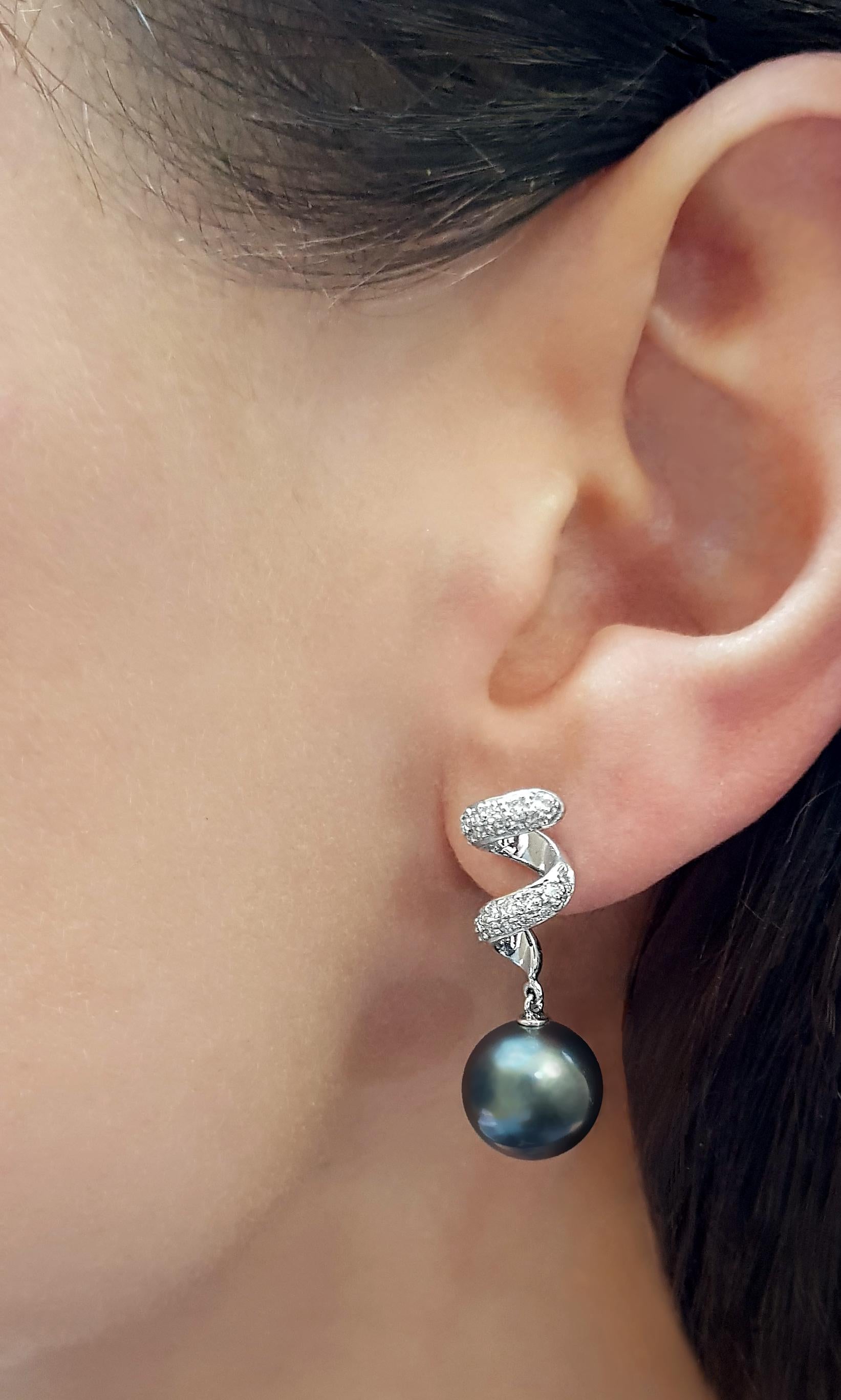These modern earrings by Yoko London feature lustrous Tahitian pearls beneath a contemporary swirl of diamonds. Set in 18 Karat white gold to enhance the rich hues of the pearls and the white sparkle of the diamonds, these earrings exude luxurious