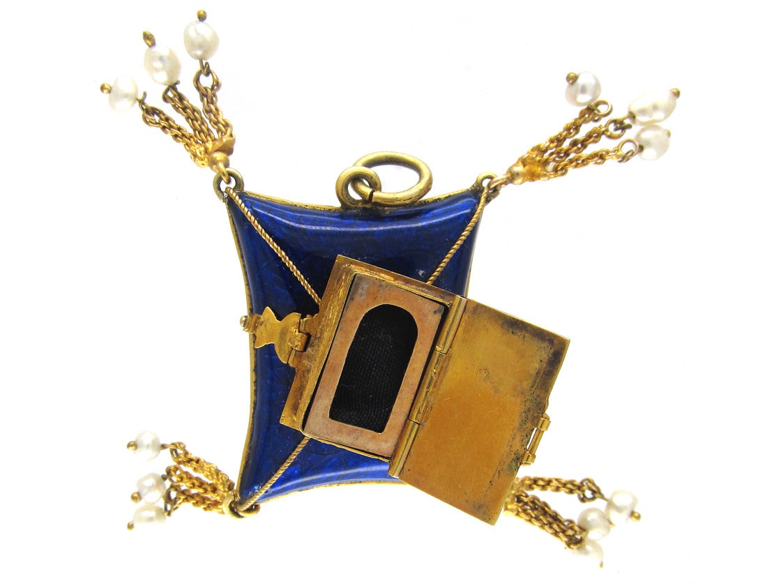 A very unusual mid-Victorian (c.1850) Royal blue enamel cushion pendant with a gold bible on top, opening to reveal a locket compartment. On the reverse is another oval locket compartment. Attached to each corner of the cushion are four triple