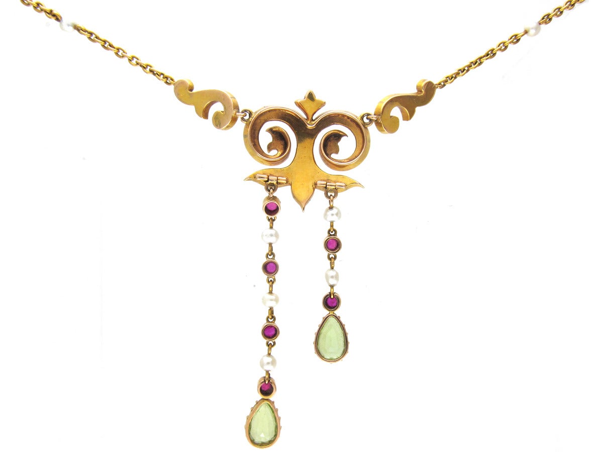 A very good quality Suffragette necklace made circa 1910. It has two uneven drops set with rubies, natural pearls and pear shaped peridots. The scroll work design joins the chain which is interspersed with natural pearls terminating in a barrel