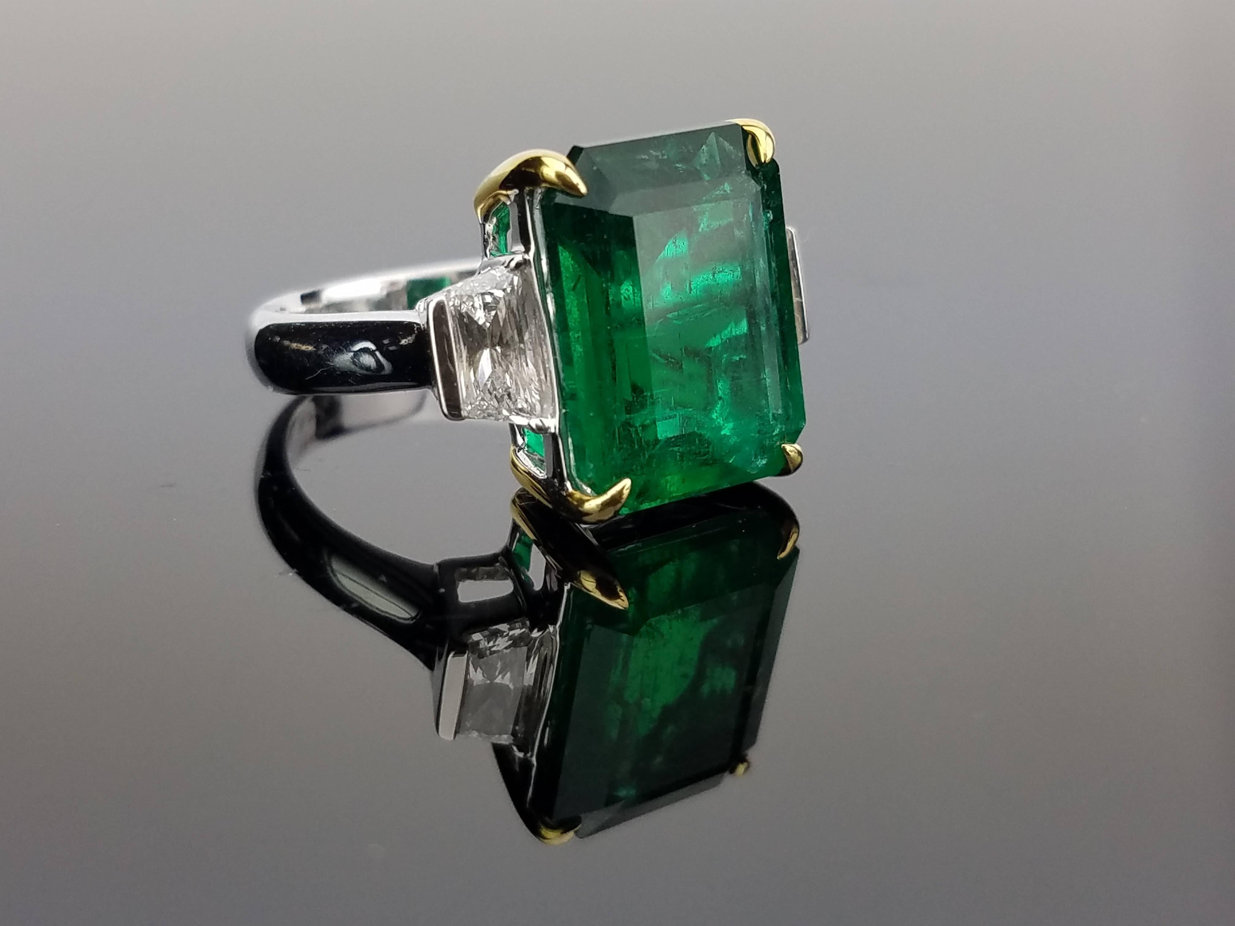 Beautiful Classic Zambian Emerald Ring with Yellow Gold prongs, and 2 Diamond side stones set in 18K White Gold hoop

Center Stone Details: 
Stone: Zambian Emerald
Cut: Emerald Cut
Weight: 8.01

Diamond Details: 
Cut: 2 x Trapezium
Total Carat