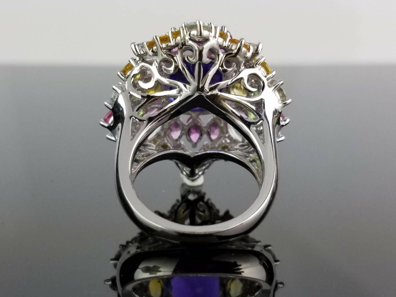 A statement cocktail ring, with a 17.65 carat Tanzanite centre stone surrounded by coloured sapphires comprising of around 25 carats. All set in 18K white gold. 

We can:
Provide a certificate upon request. 
Change ring size upon request (with no
