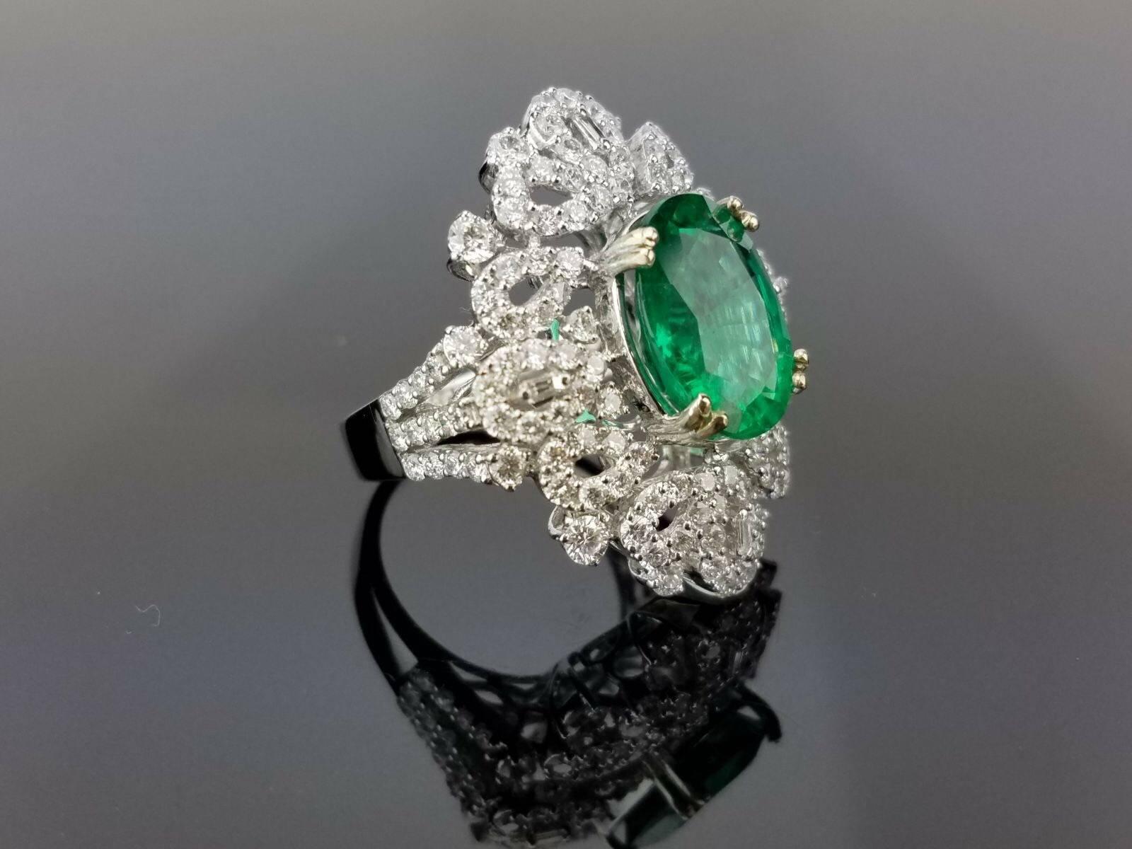 An eye-catching cocktail ring, with a beautiful emerald centre stone embellished with white diamonds, all set in 18K white gold. 

Stone Details: 
Stone: Emerald
Cut: Oval
Carat Weight: 4.95 Carat

Diamond Details:
Total Carat Weight: 2.94