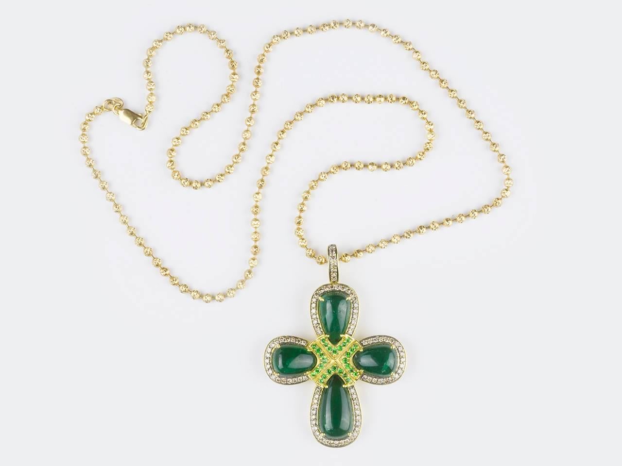 Pendant features 4 pear-shaped emerald cabochon emeralds in colored diamond-set frames and round garnets with blackened gold accents. Signed WINC. (Robert Wander). Cross is suspended from gold ball-link chain.