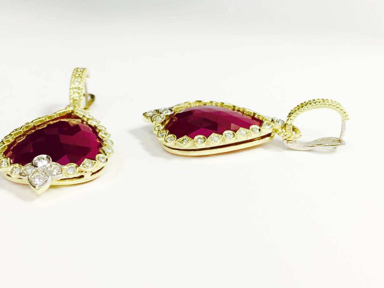 18K Gold Earrings w/ Pear-Shape, Rose-Cut Ruby centers surrounded by white diamonds.

1.30 ct.'s of G Color, VS Quality Diamonds

Top clasp is covered in diamonds and clip-on back makes this an easy wear

Back pattern is flowers and piece is