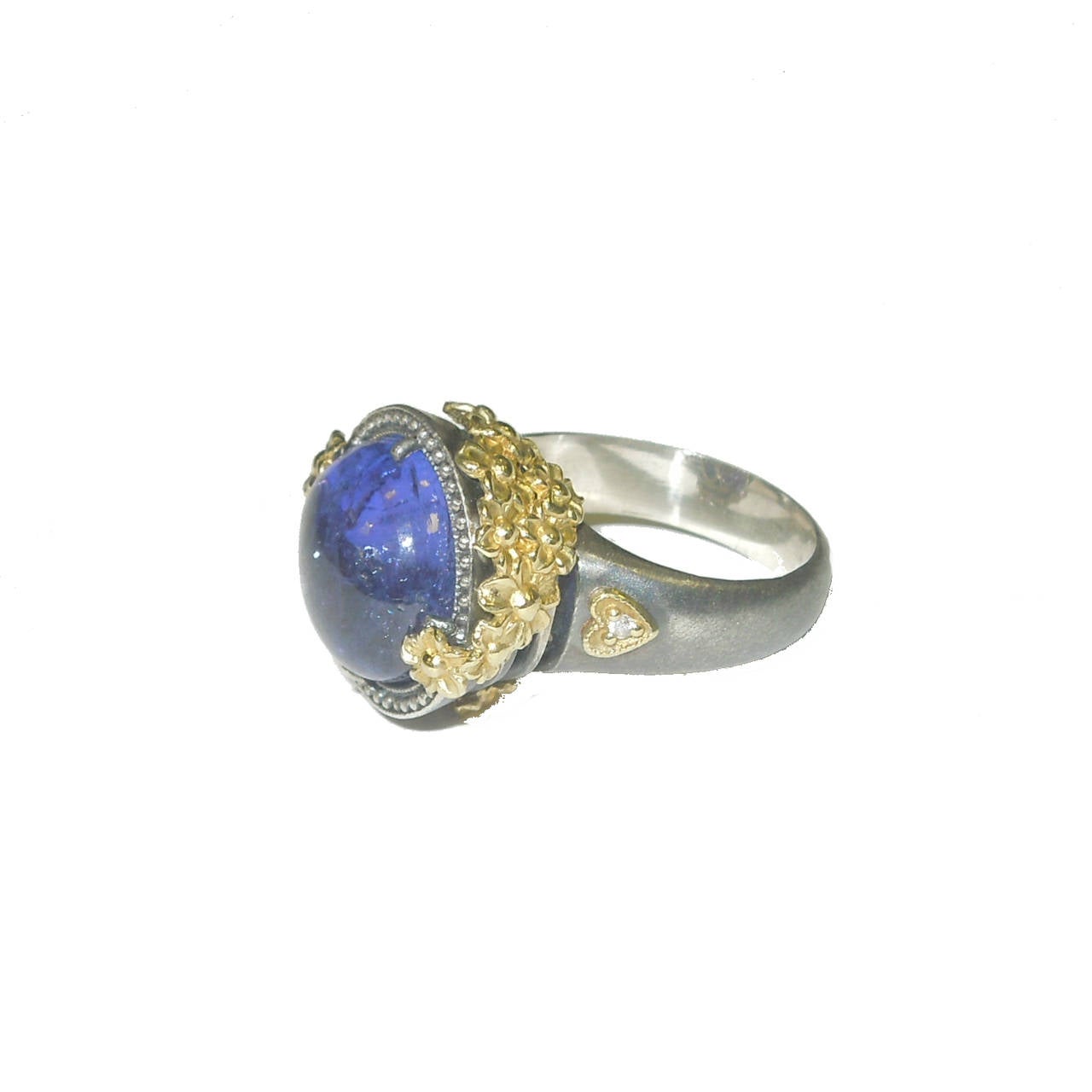 Aged Silver & 18K Gold Ring w/ Cabochon Tanzanite Center

18K Gold Flowers cover the sides of the ring with unique detail

Center Cabochon Tanzanite 8.95 ct.'s

Side of the ring has our Trademark 