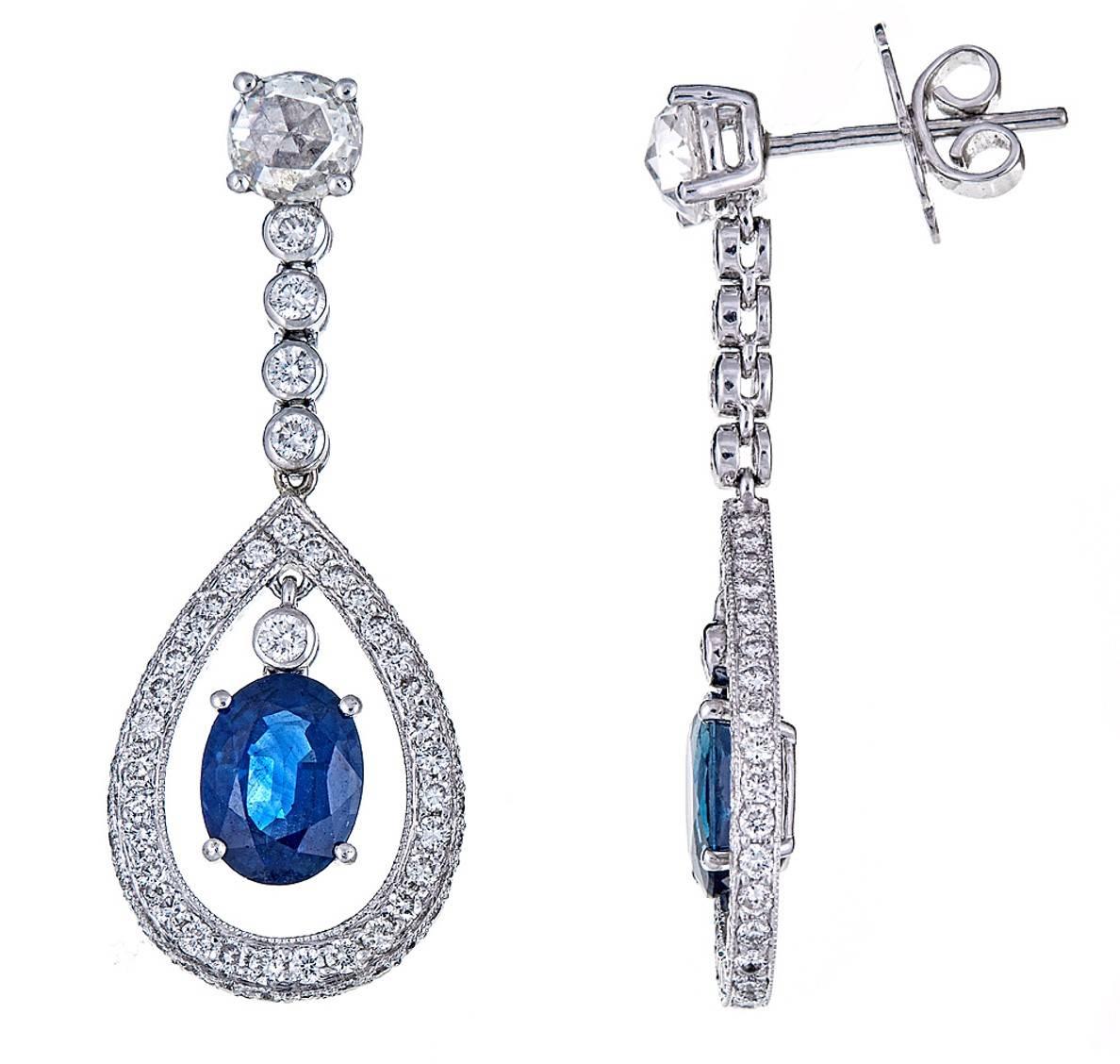 A breathtaking pair of 18K White Gold drop earrings. Two larger, round diamonds, cascade downward into pave diamond enhanced drops for a combined weight of 2.28 carats. Within the center, 3.30 carats of bright, oval Blue Sapphires hang delicately. 