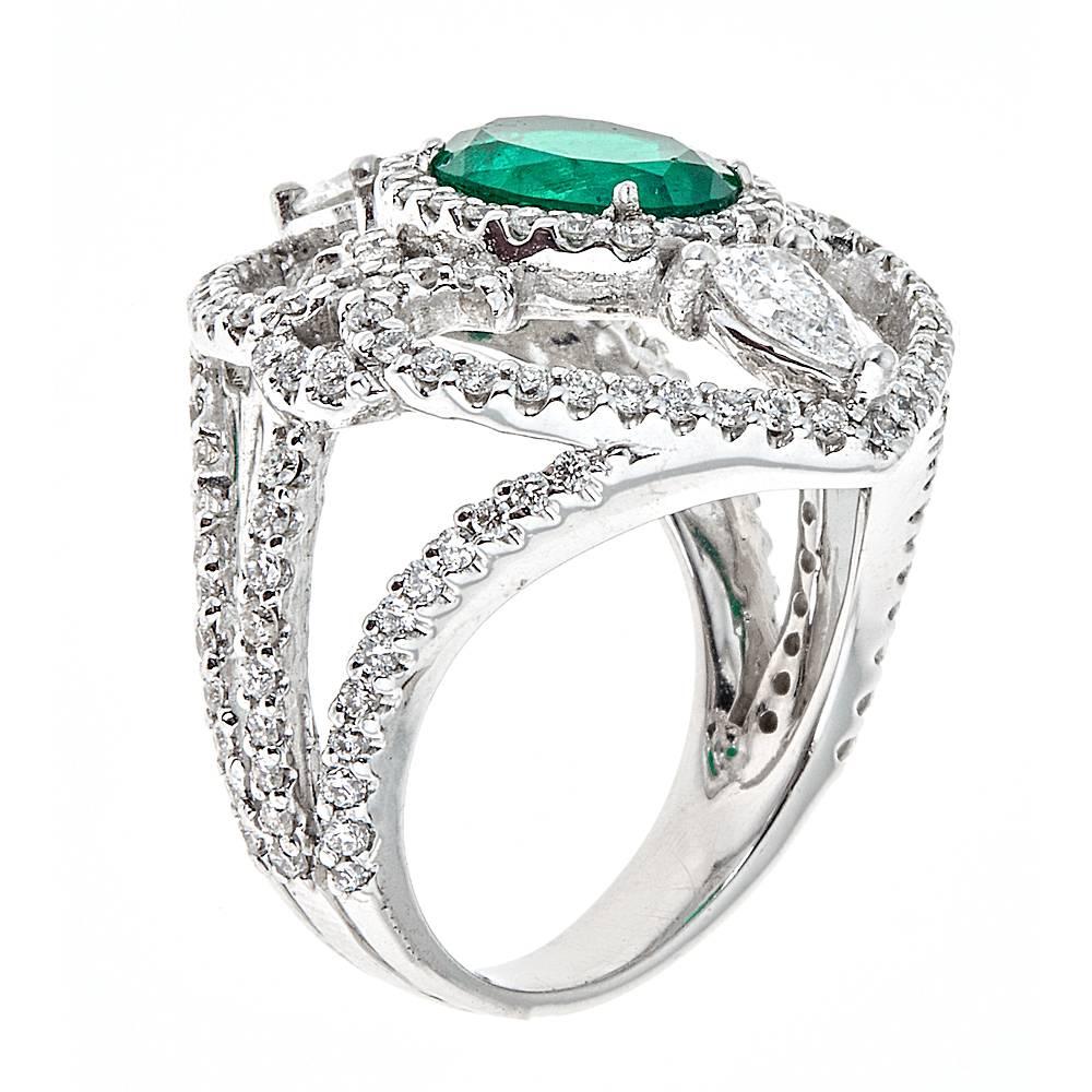 Featuring a magnificent 1.66 carat center oval Emerald, this exquisitely designed cocktail ring is set in 18K White Gold. Complimenting the vibrant green emerald are flourishes of round and pear shaped white Diamonds. With an intricately designed