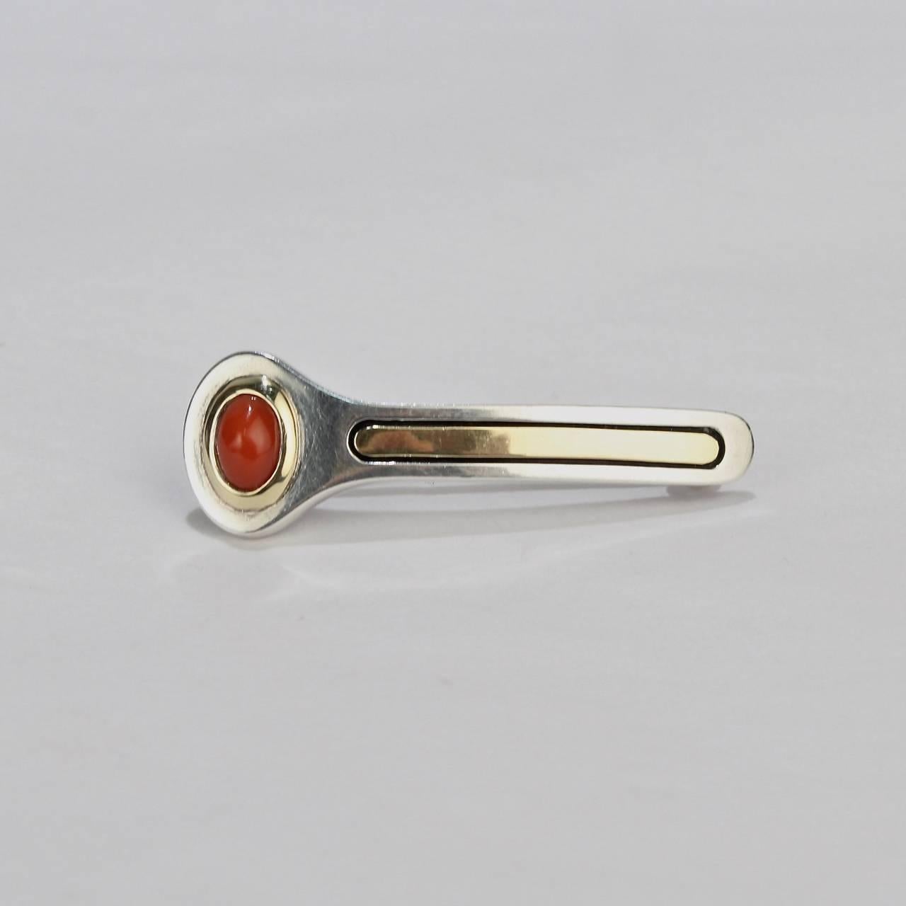A fine, modernist brooch or lapel pin by Cartier.

Comprised of sterling silver, 18-karat yellow gold, and set with a salmon red coral cabochon. 

A wonderful brooch with both simple & modern lines. 

Marked on the reverse: Cartier / 925 /