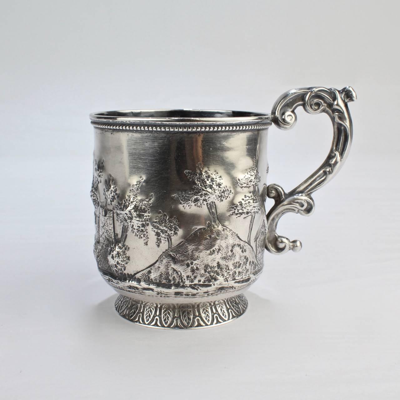 An truly special mid-19th century New Orleans coin silver mug made by Adolphe Himmel. The mug depicts a landscape and architectural scene with a hills, houses, the ruins of a castle or fort, trees, and abundant plant life.

The mug was retailed by