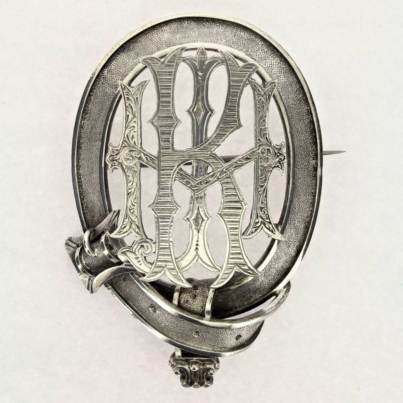 A large figural Victorian silver buckle brooch with a monogram. 

The brooch retains its original fitted box. 

The reverse is unmarked. The silver will likely grade as either coin silver or sterling silver. 

Condition:
It is in overall good,