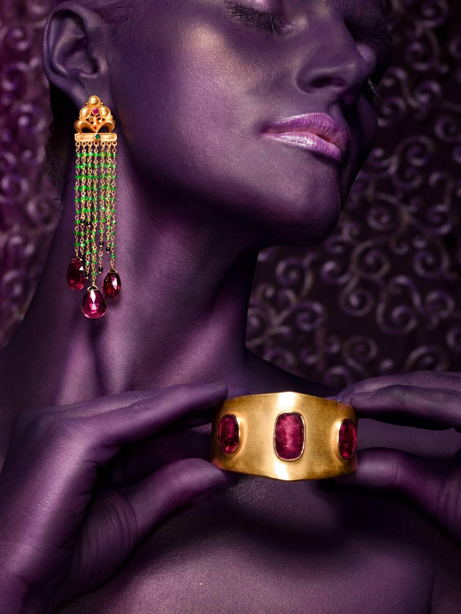 A pair of spectacular and unique, hand crafted 18 karat gold precious stone earrings. Dark red Tourmaline drops are suspended by vibrant green tsavorite beads. Small onyx beads are playfully dispersed among the tsavorite which are held by an 18