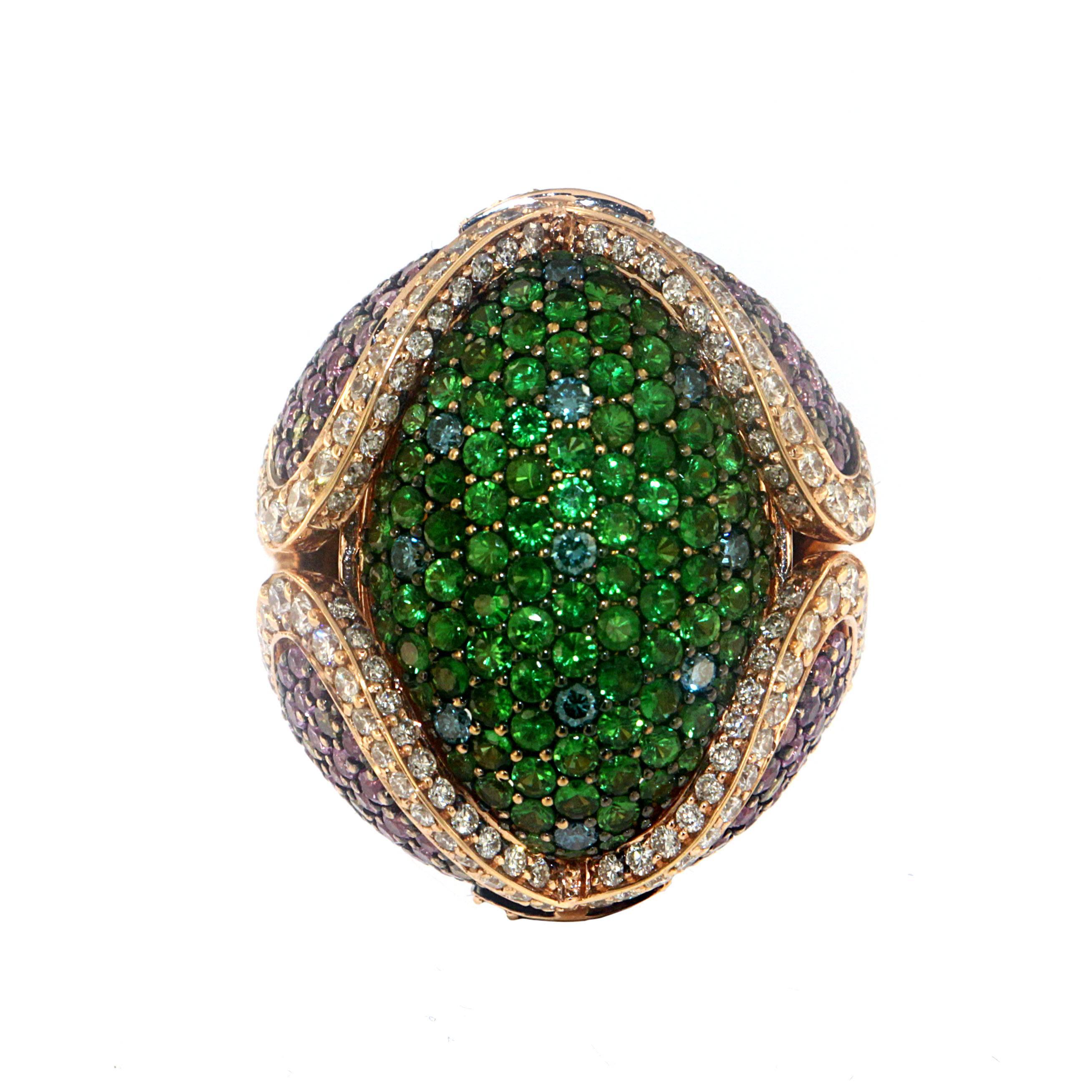 This bombe cocktail ring is a triumph of colorful precious gemstones featuring 2.92 Carats of Tsavorite Garnet at the dome with 3.69 Carats of Pink Sapphires, 1.60 Carats of White Diamonds, and 0.33 Carats of treated Blue Diamonds set on a pave-set