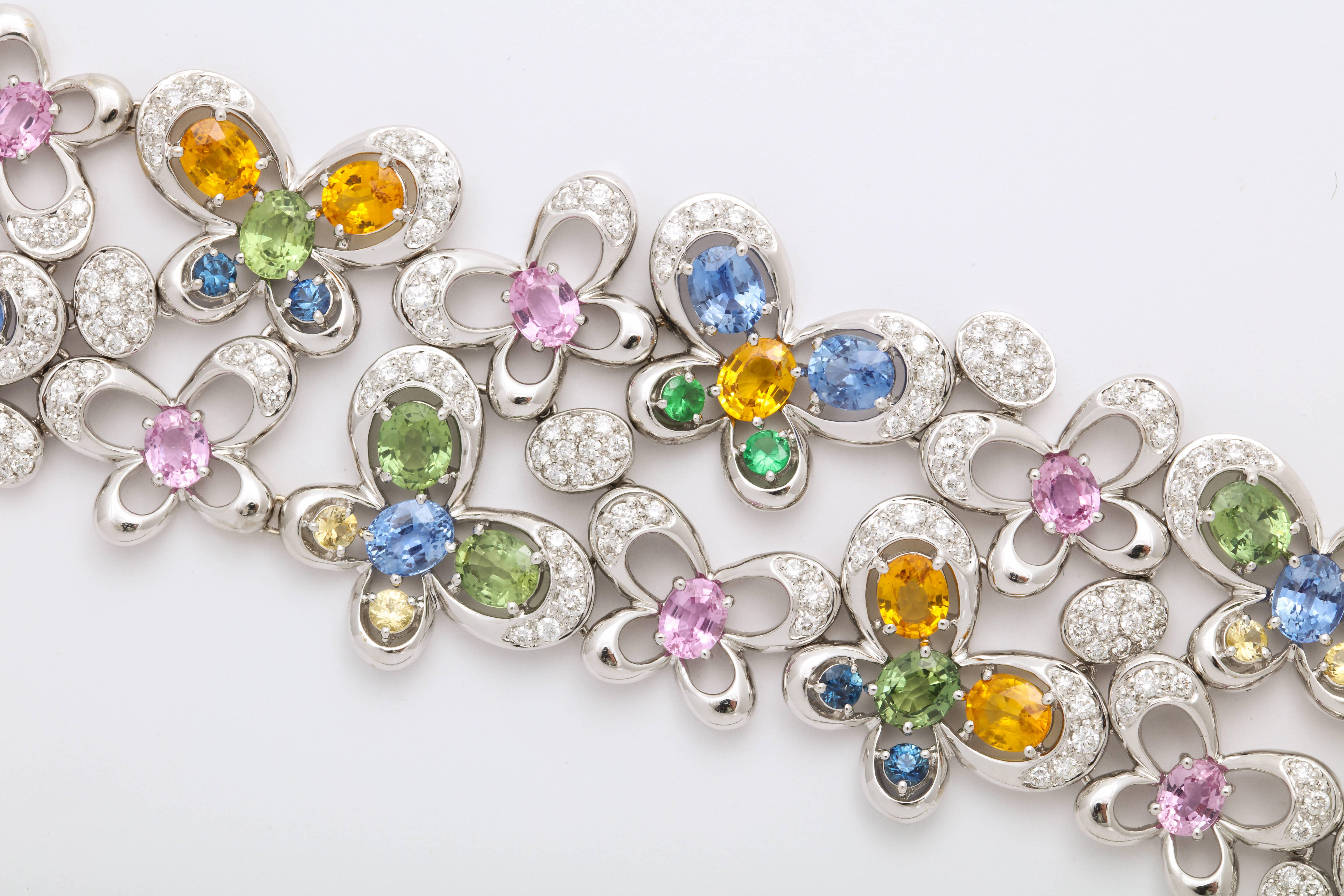 Festive 18 Karat White Gold articulating strap bracelet mounted with oval faceted blue and green sapphires: 2.96 carats; and pink and yellow sapphires: 7.73 carats, in the form of butterfly motifs, with staggered tsavorites (green garnets),