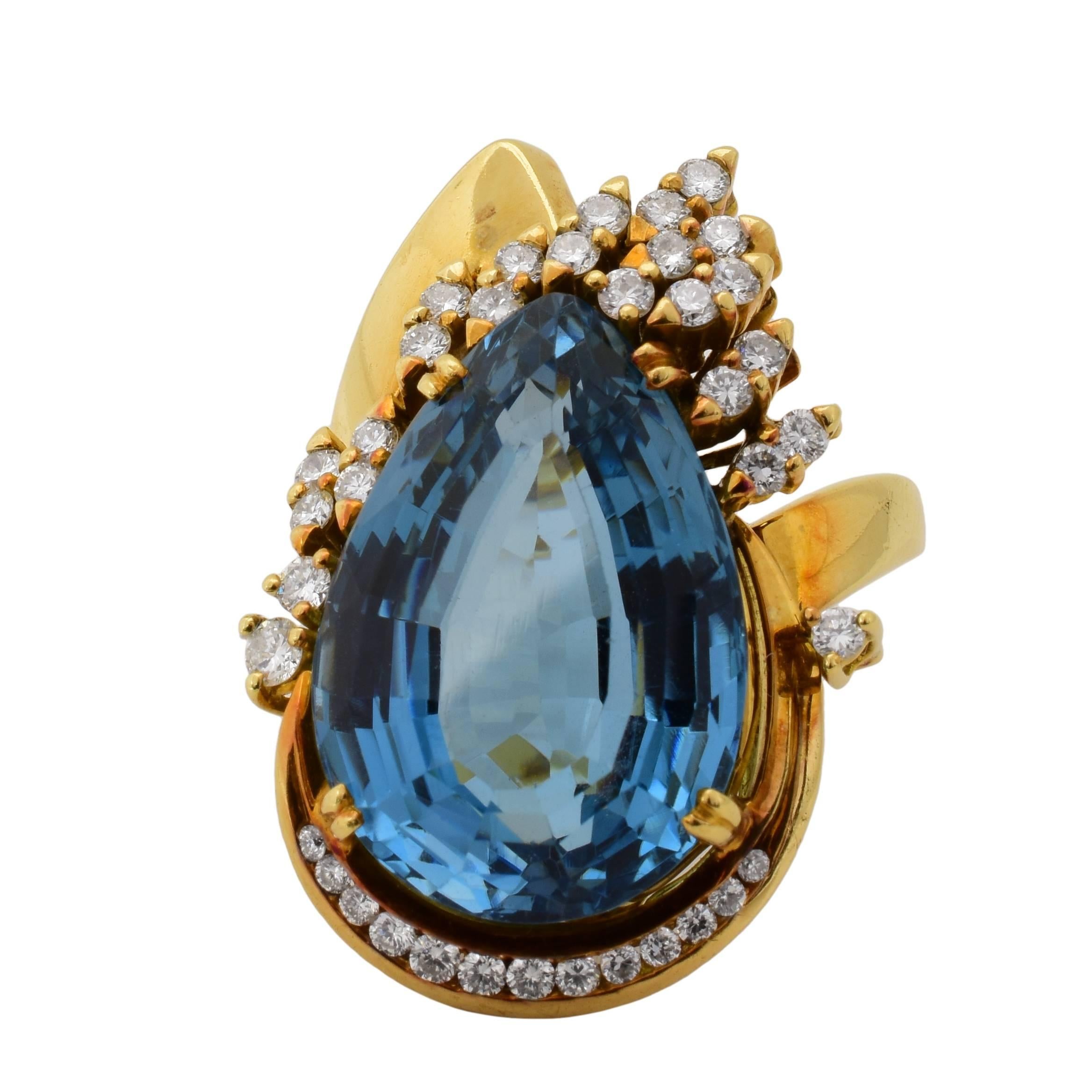 This 1940's cocktail ring features an approximately 20 carat pear shape blue topaz center stone, accented by a cluster of diamonds, in an 18k yellow gold Retro mounting. 