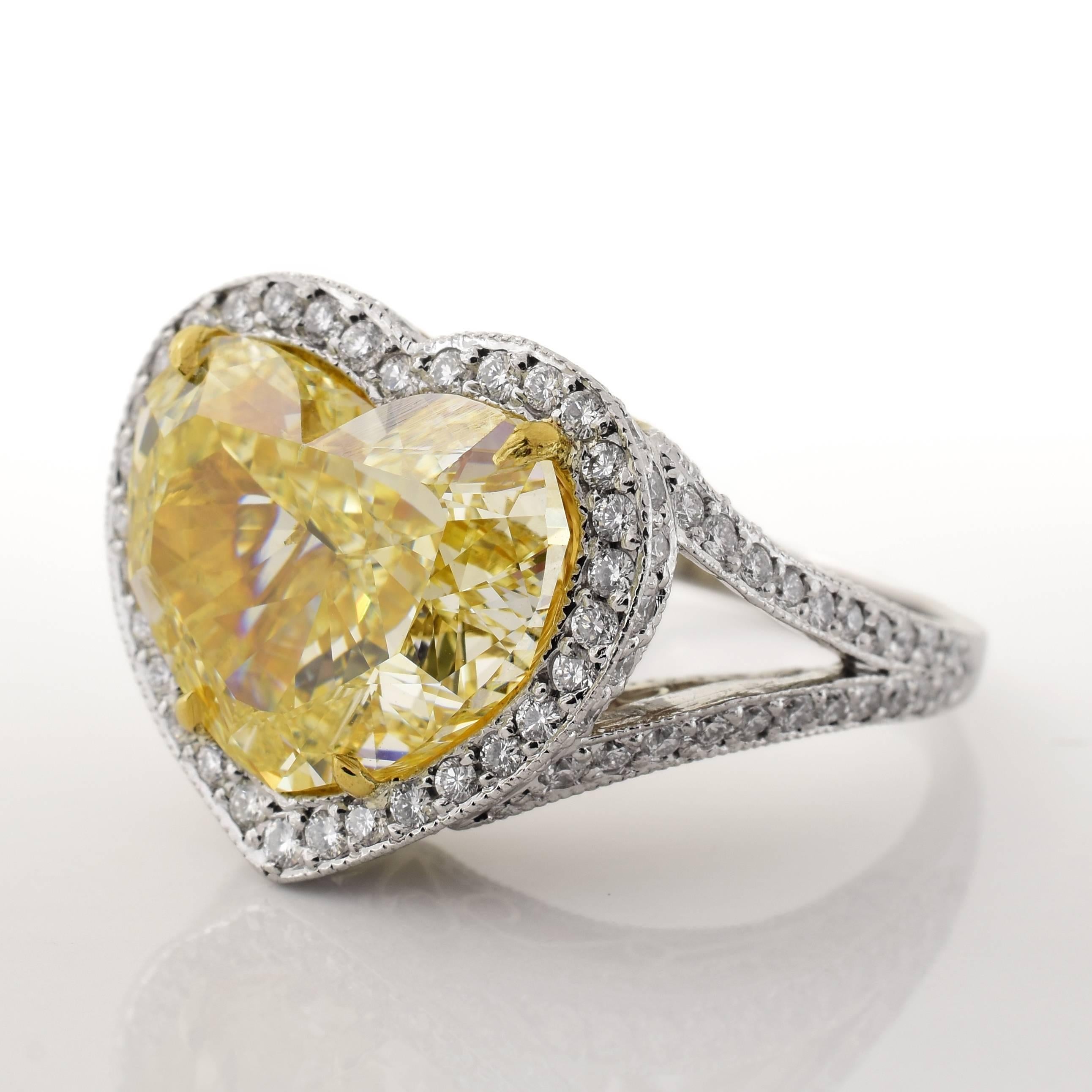This ring features a 7.12 carat SI1 fancy yellow heart shaped diamond center stone. The heart is surrounded in white accent diamonds, with prongs and details in yellow gold, with the rest in platinum. The ring is a size 6.25 US.